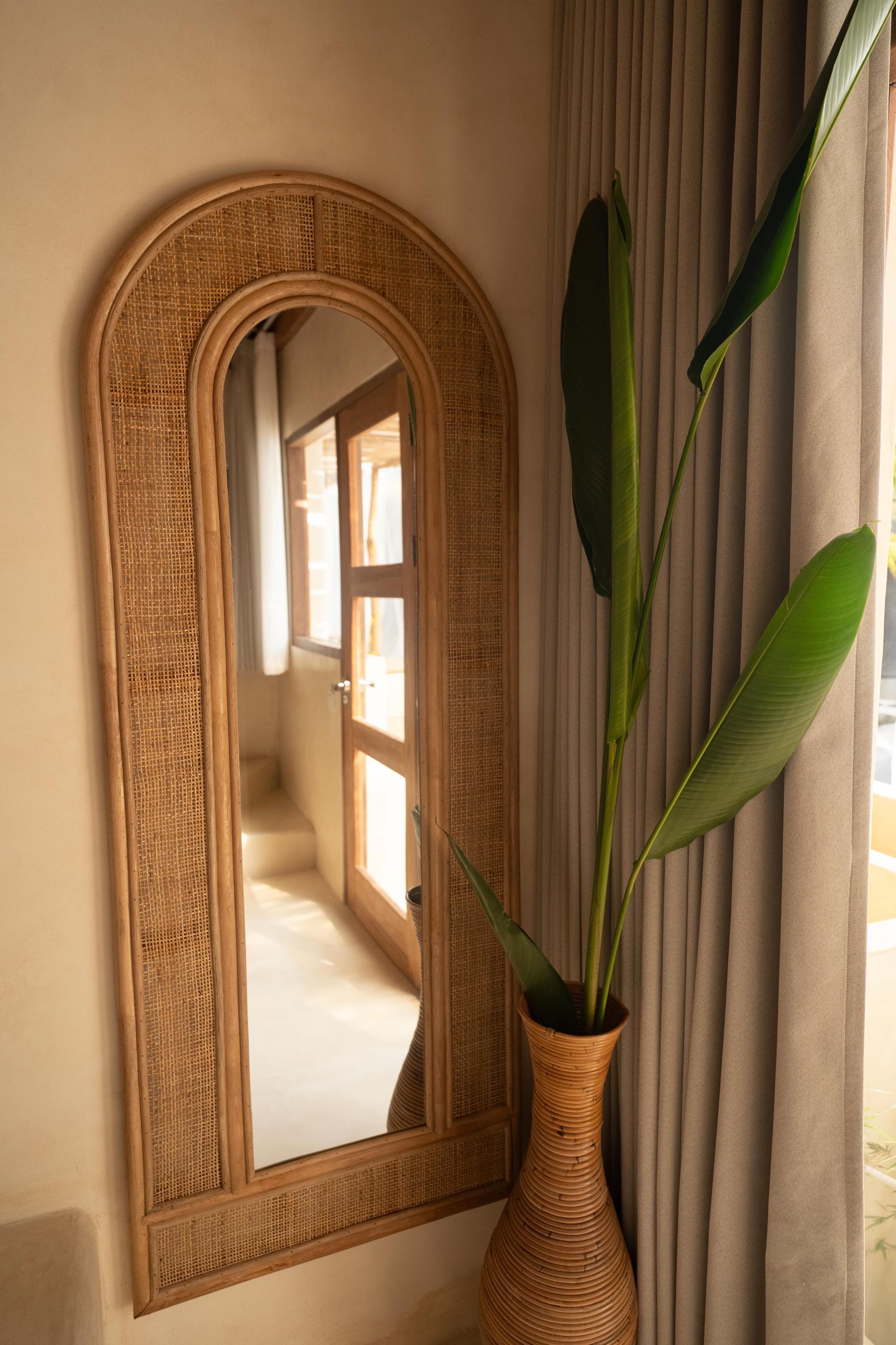 A large mirror is hanging on a wall next to a vase with a plant in it.
