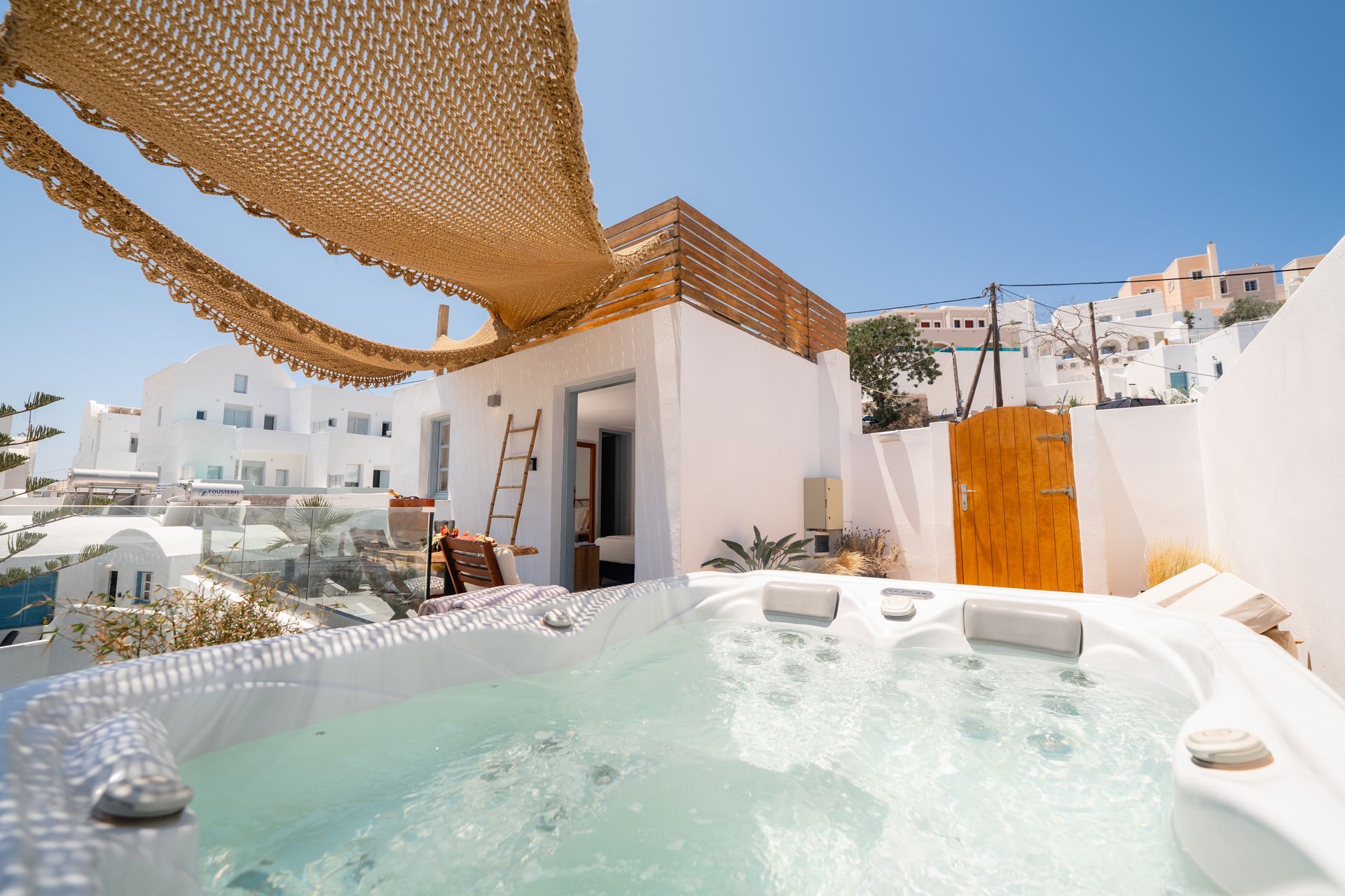 Luxury rooftop hot tub with sunshade, white walls, and ocean-view terrace under a clear blue sky
