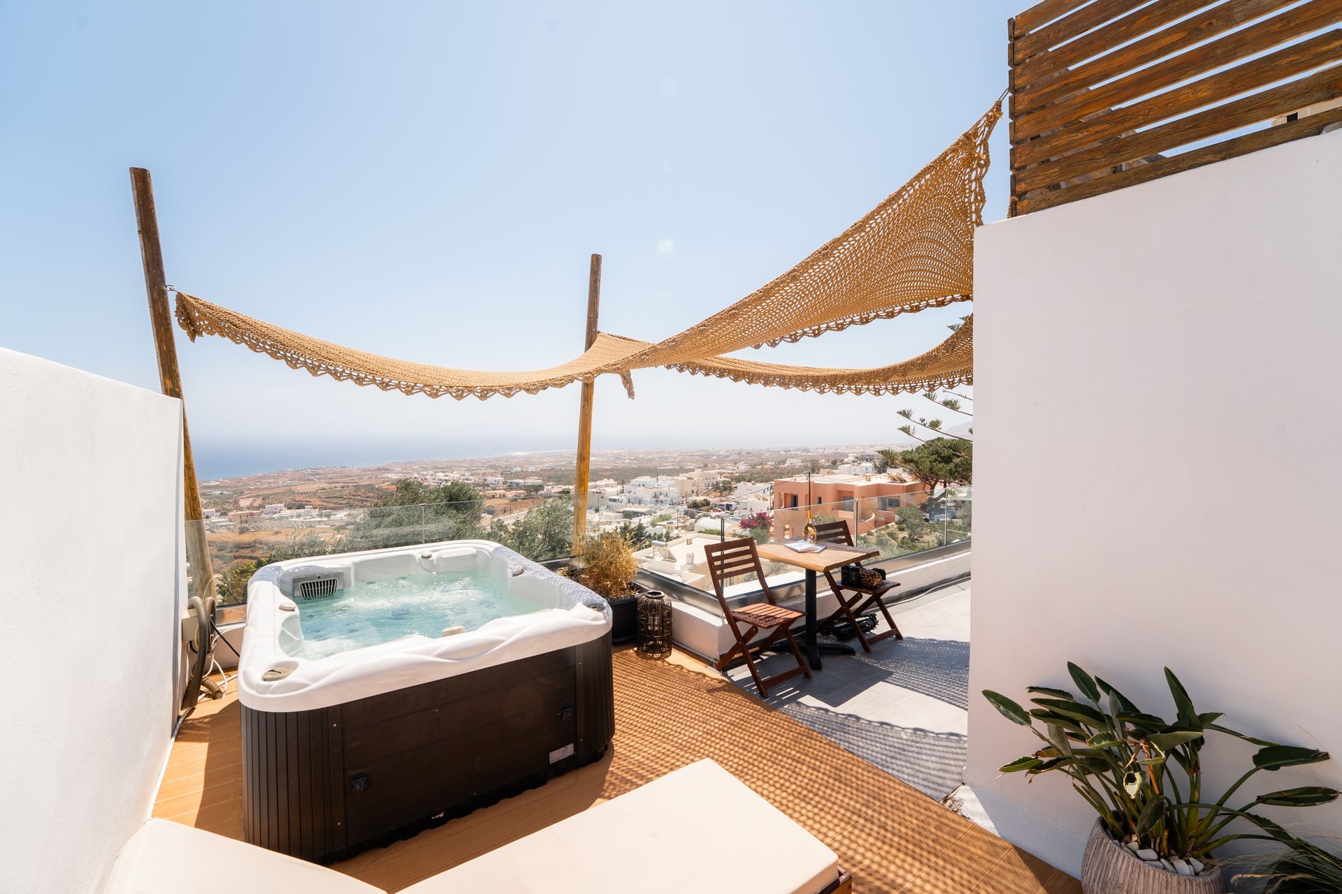 Rooftop patio with hot tub overlooking city, sun shade, table and chairs, sunny day.