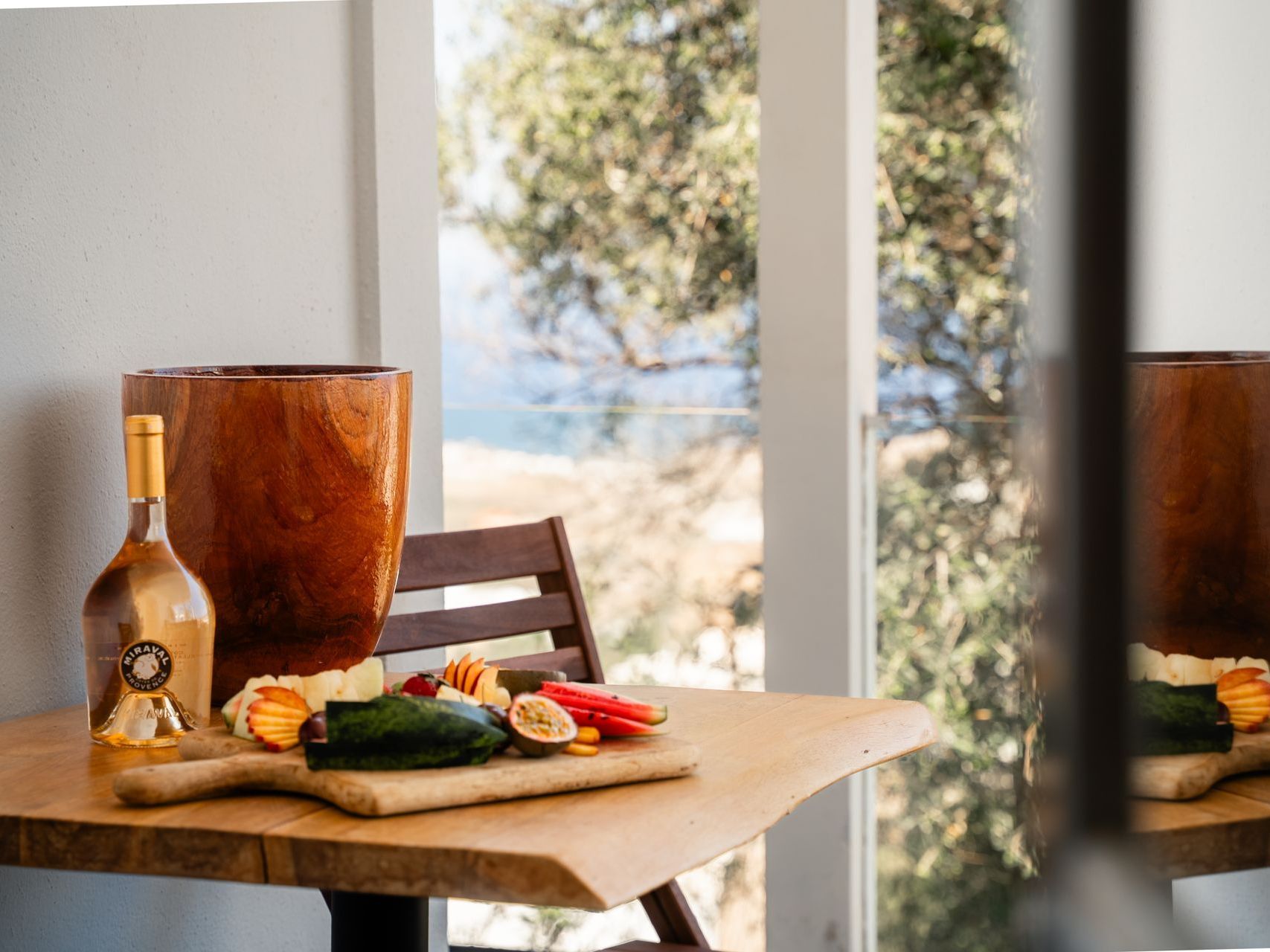 Table set with veggies and wine by a window overlooking an ocean view.