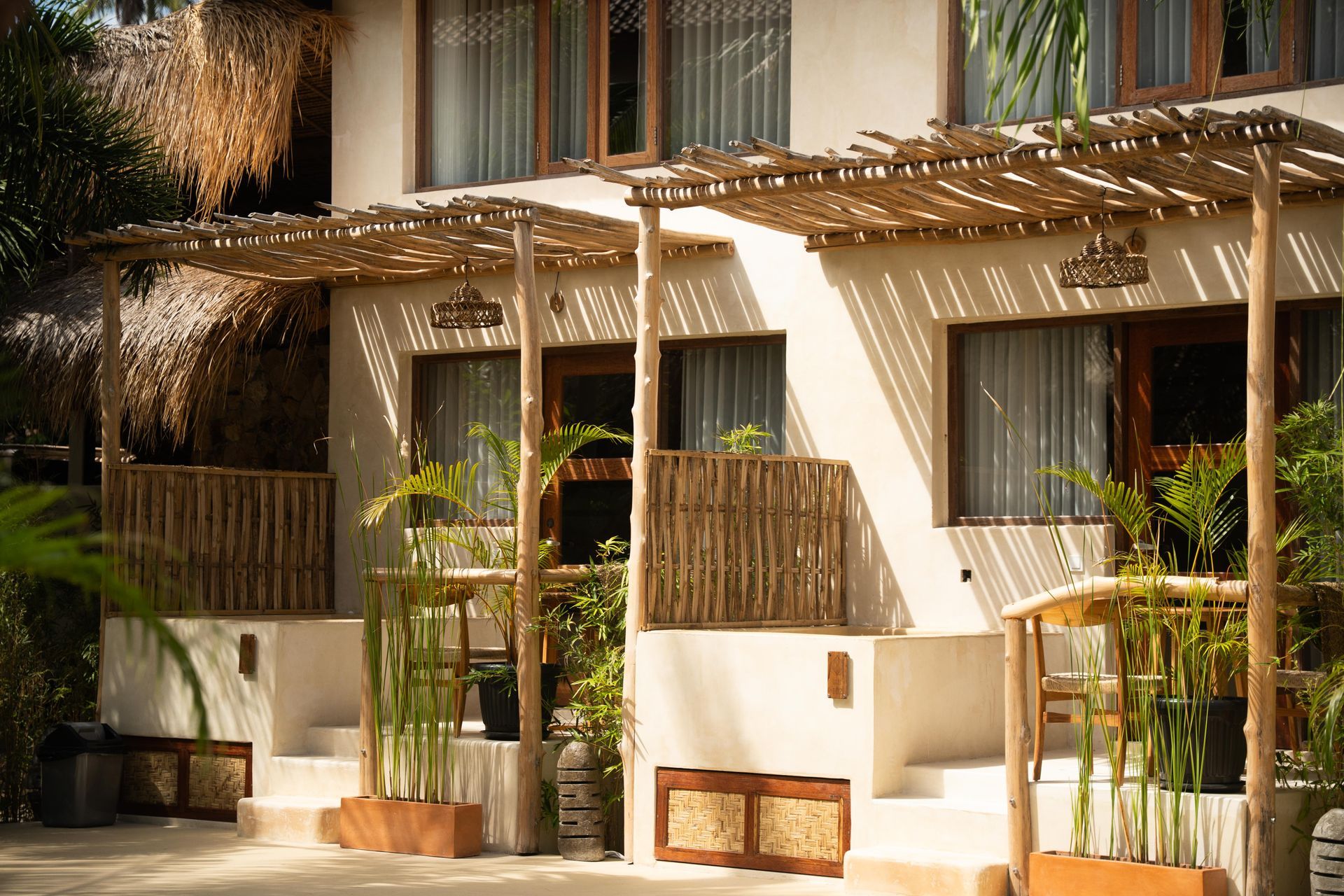 Two-story white buildings with bamboo awnings and thatched roofs, tropical setting.