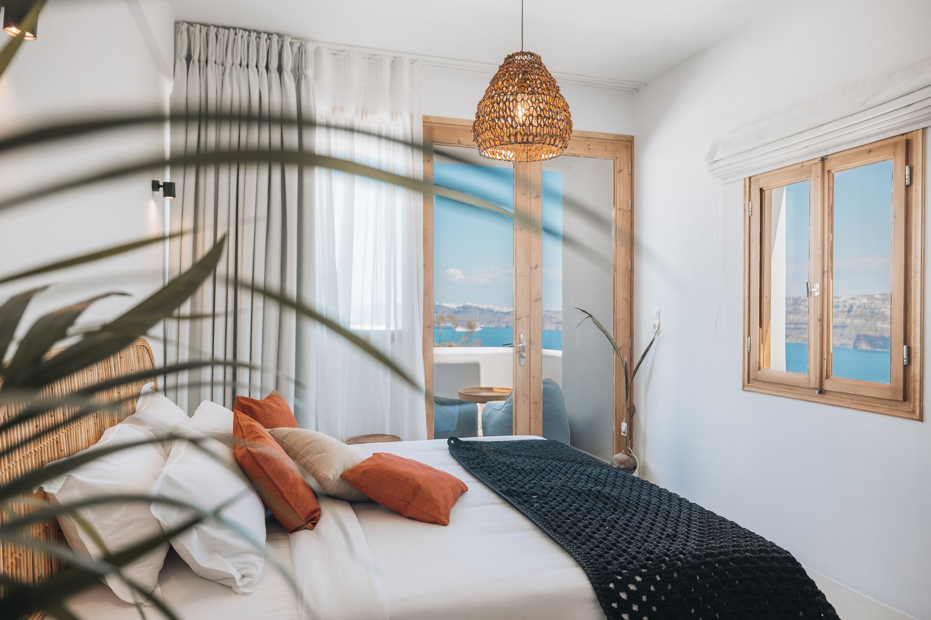 A bedroom with a king size bed , two windows and a balcony overlooking the ocean.