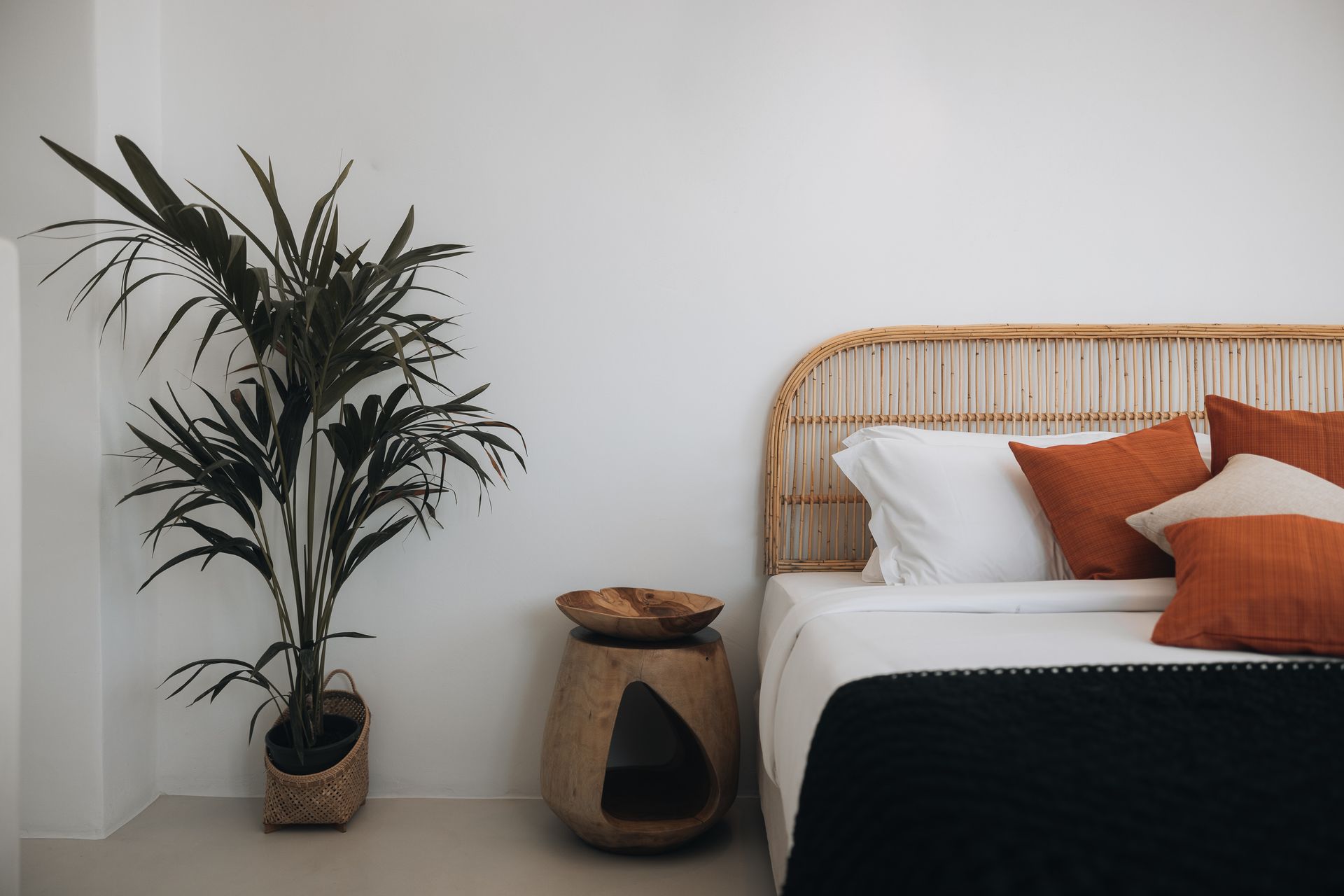 A bedroom with a bed , nightstand , plant and wicker headboard.