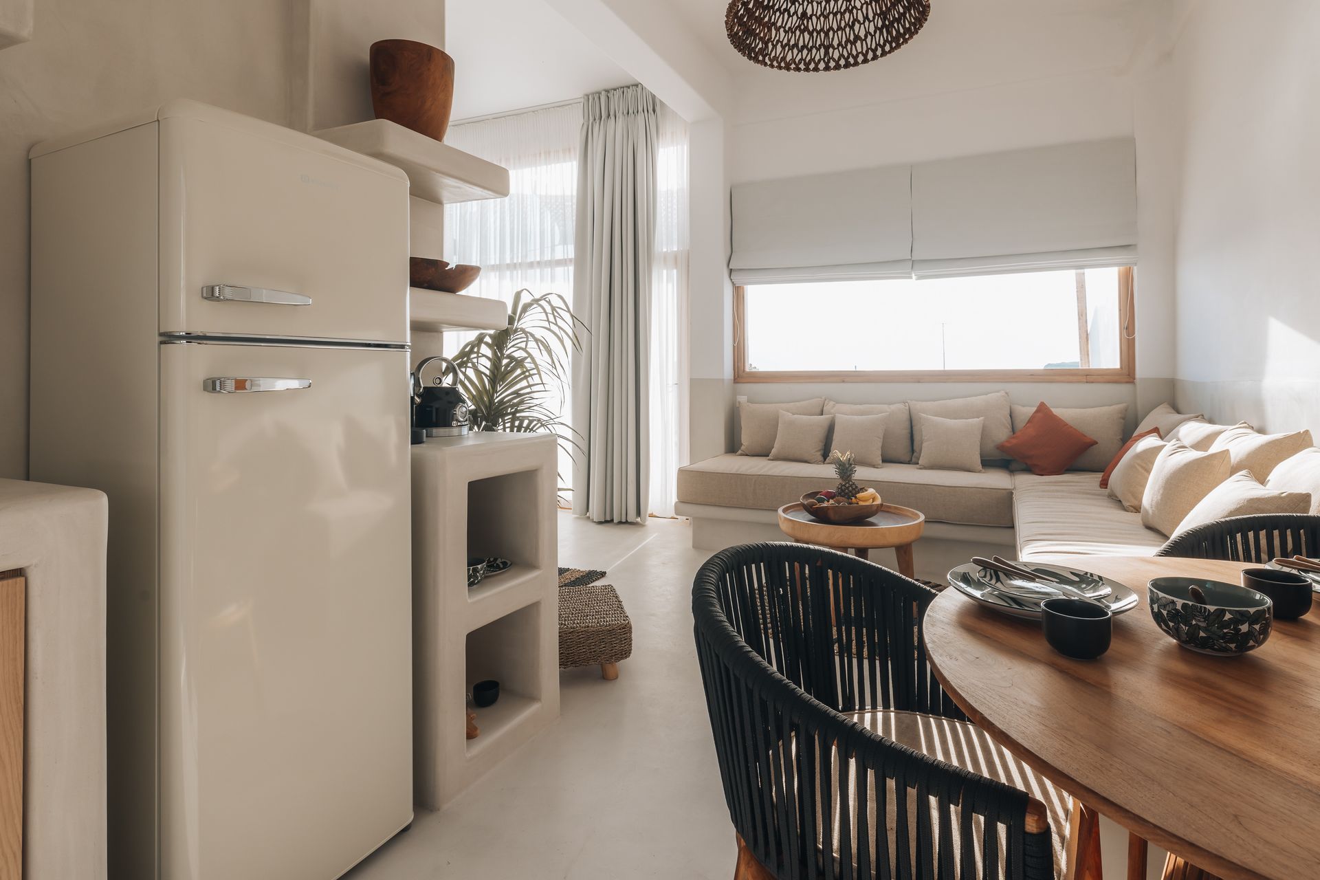 A living room with a couch , table , chairs and a refrigerator.