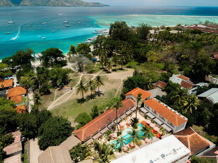 Aerial view of a coastal resort with a pool, trees, and turquoise water.