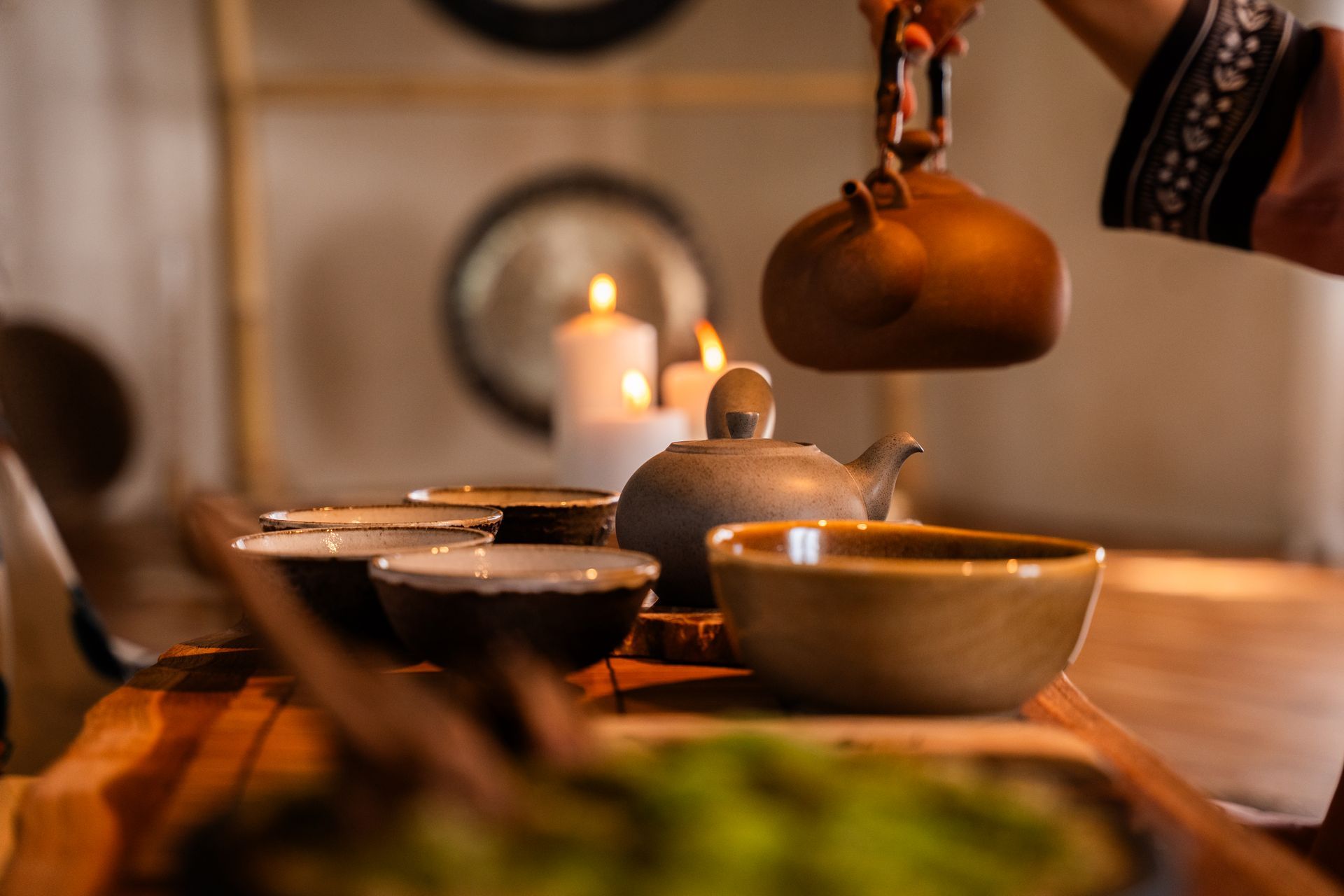 Tea ceremony with teapot, bowls, and candles on a wooden tray; person pouring tea.