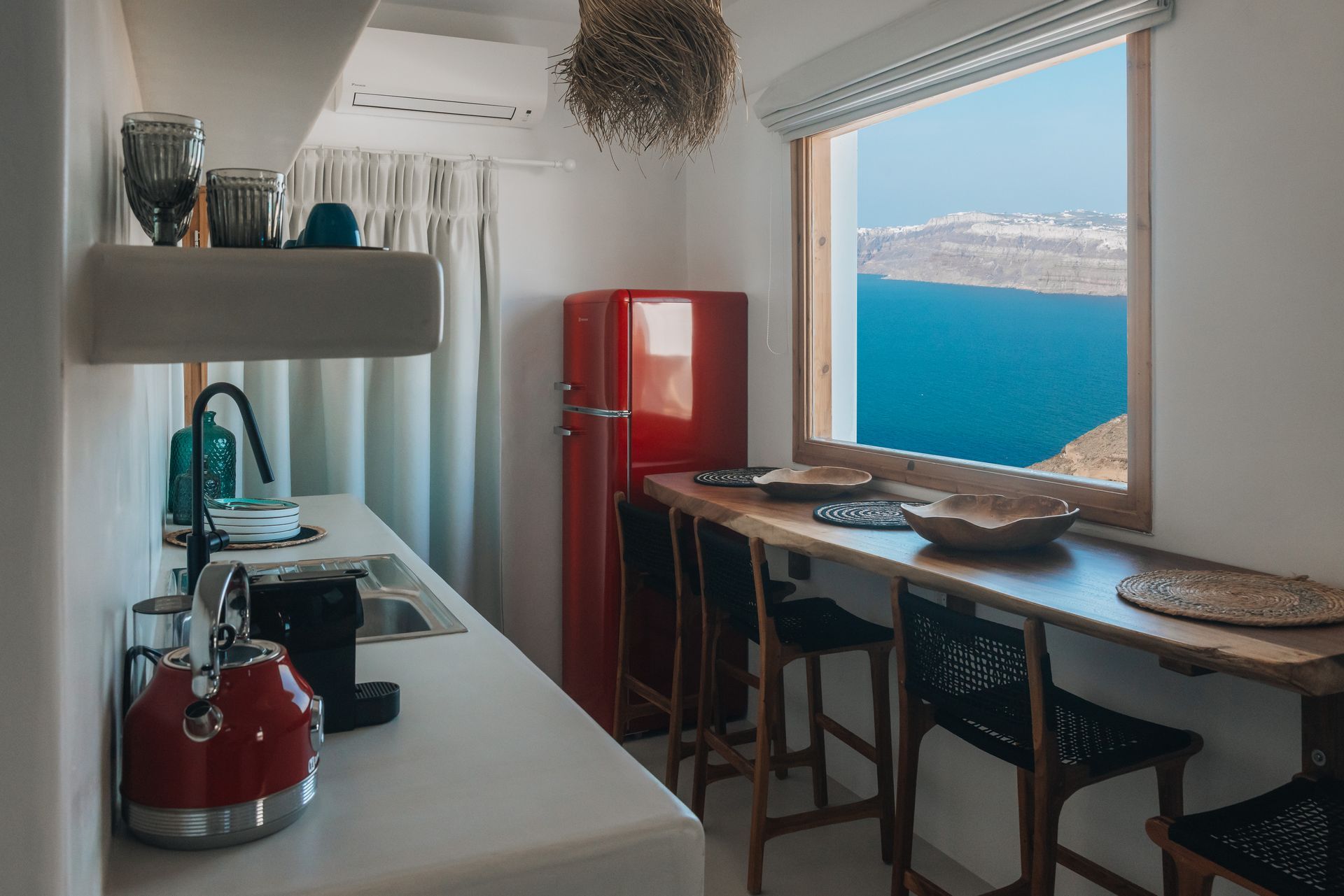 A kitchen with a red refrigerator and a table with a view of the ocean.