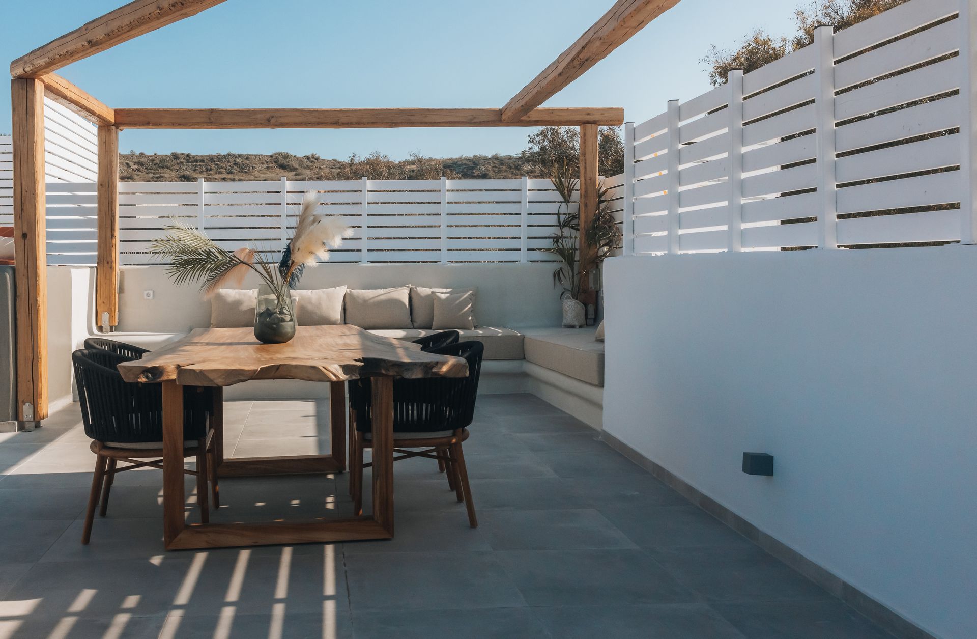 A patio with a wooden table and chairs under a pergola.