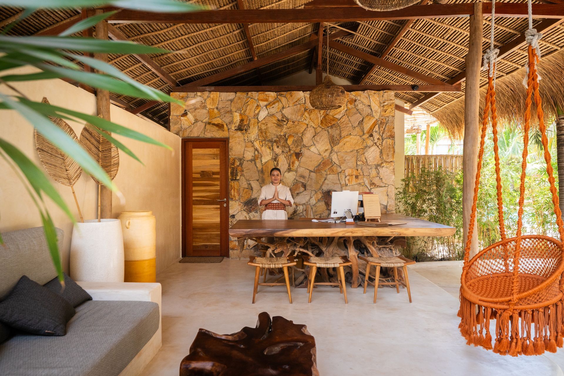 Reception area with wood desk, stone wall, and macrame swing. A person stands behind the desk.