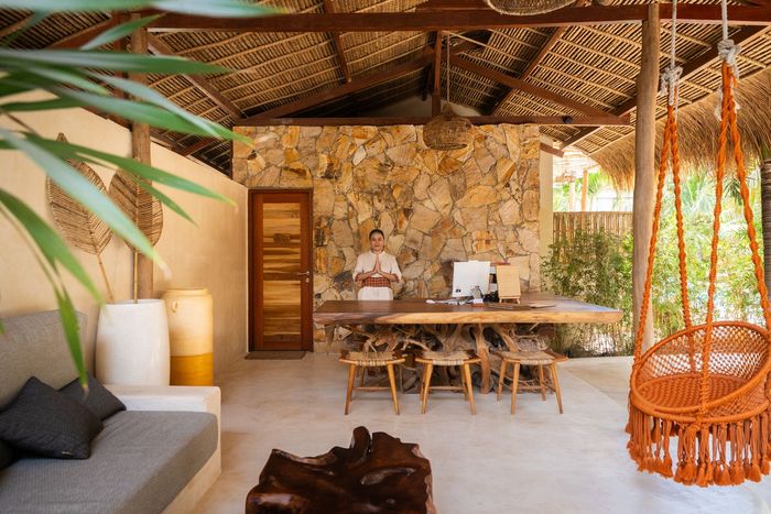 Reception area with wood desk, stone wall, and macrame swing. A person stands behind the desk.