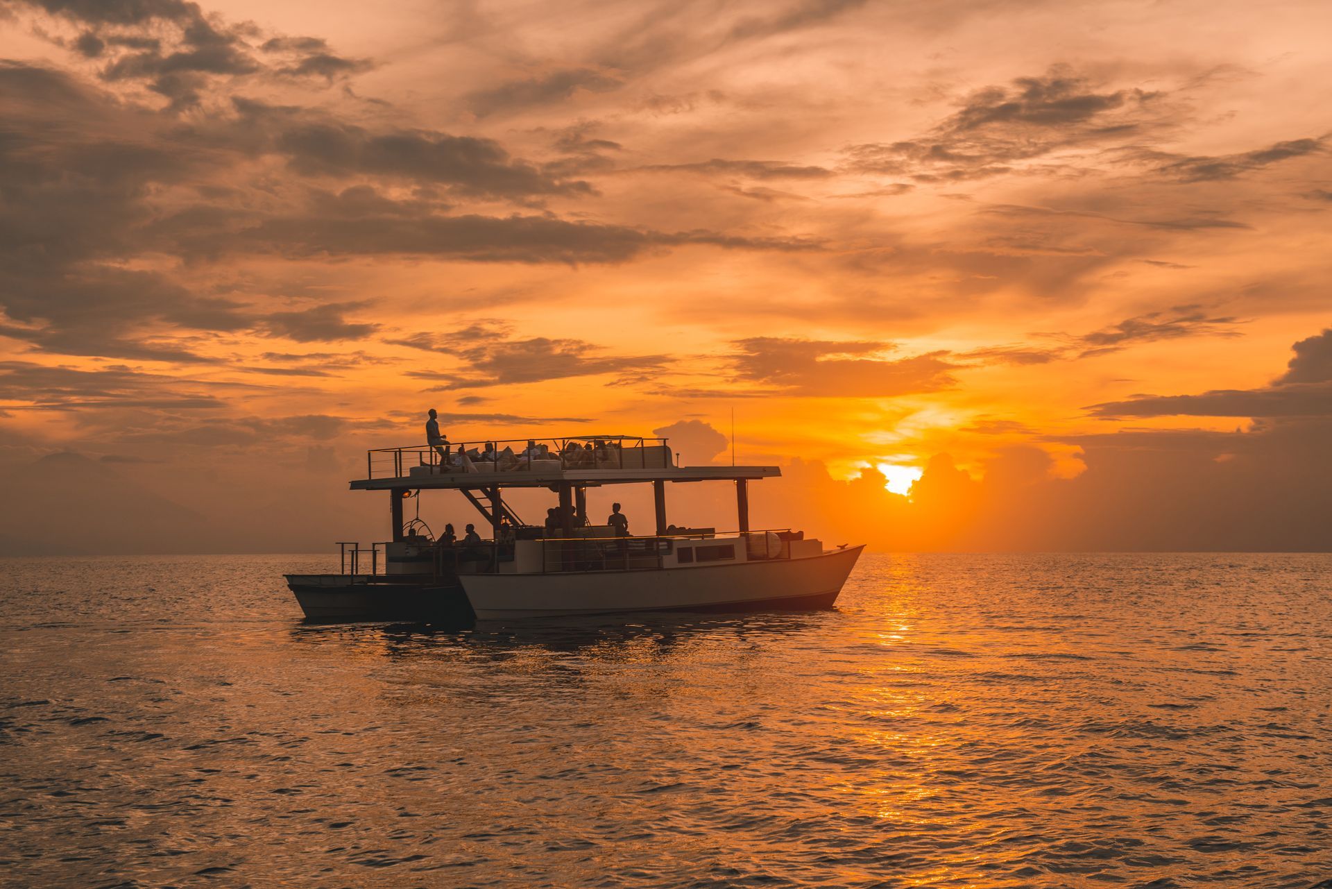Boat silhouetted on calm water at sunset, with orange sky and glowing sun on the horizon