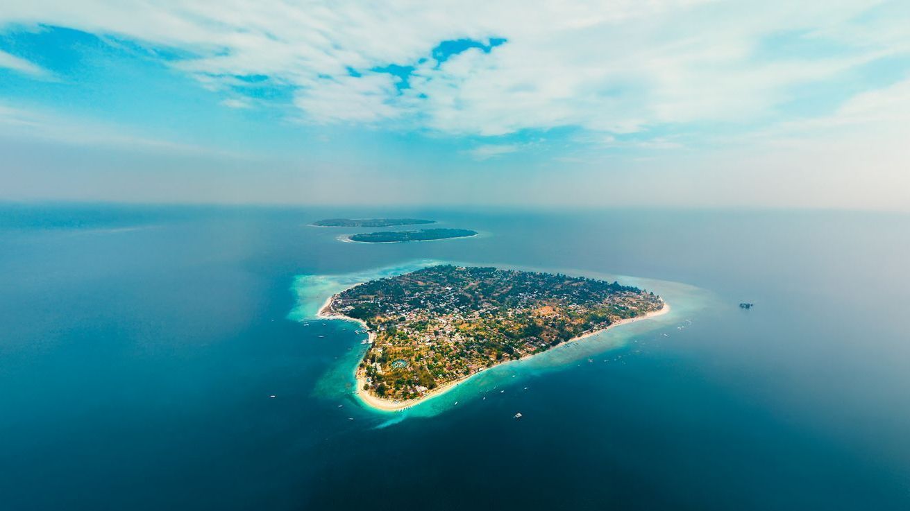 Aerial view of a lush green island surrounded by turquoise water under a blue sky with fluffy clouds.