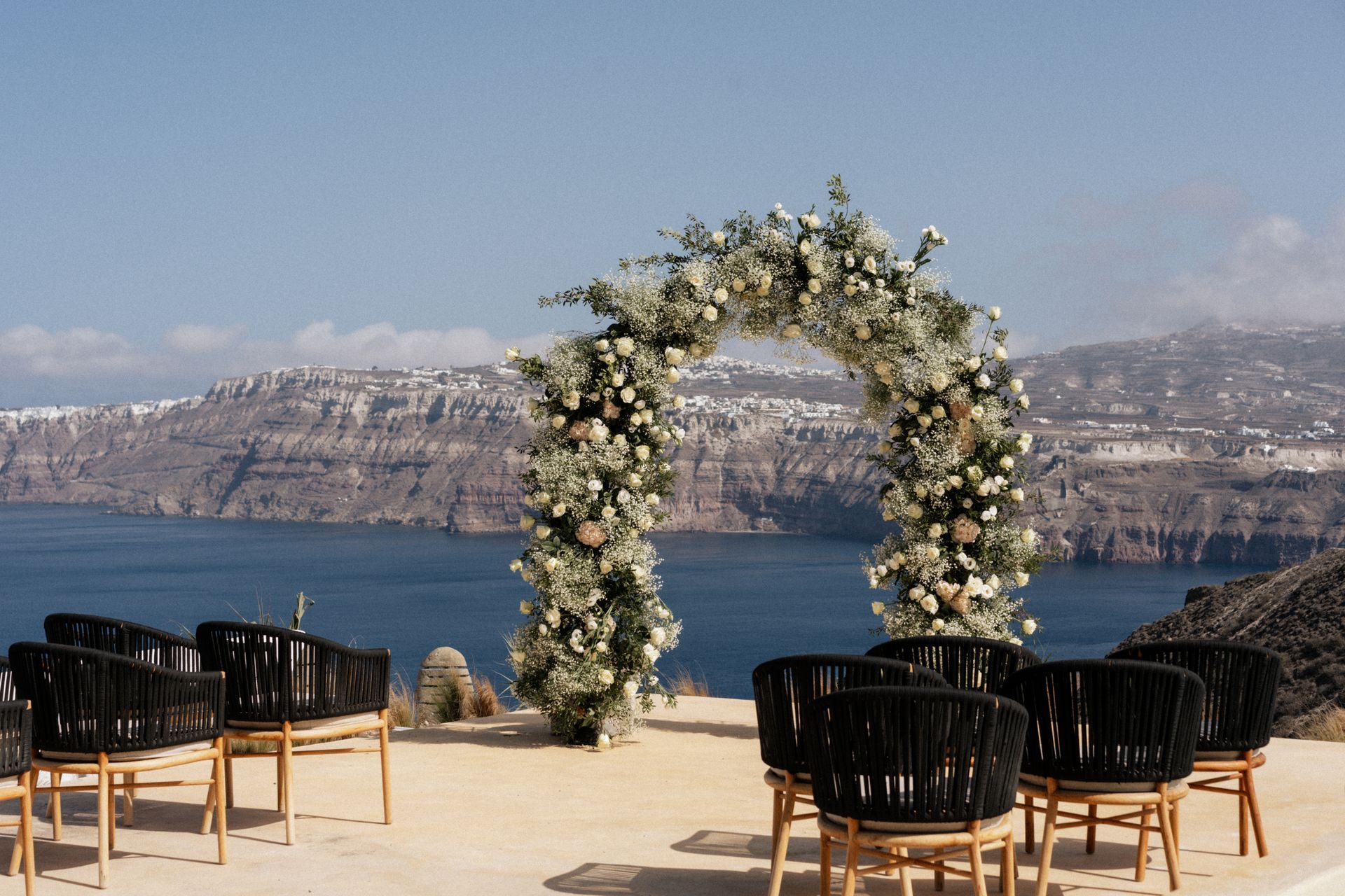 Wedding arch decorated with flowers overlooking the sea, with chairs set up for guests.