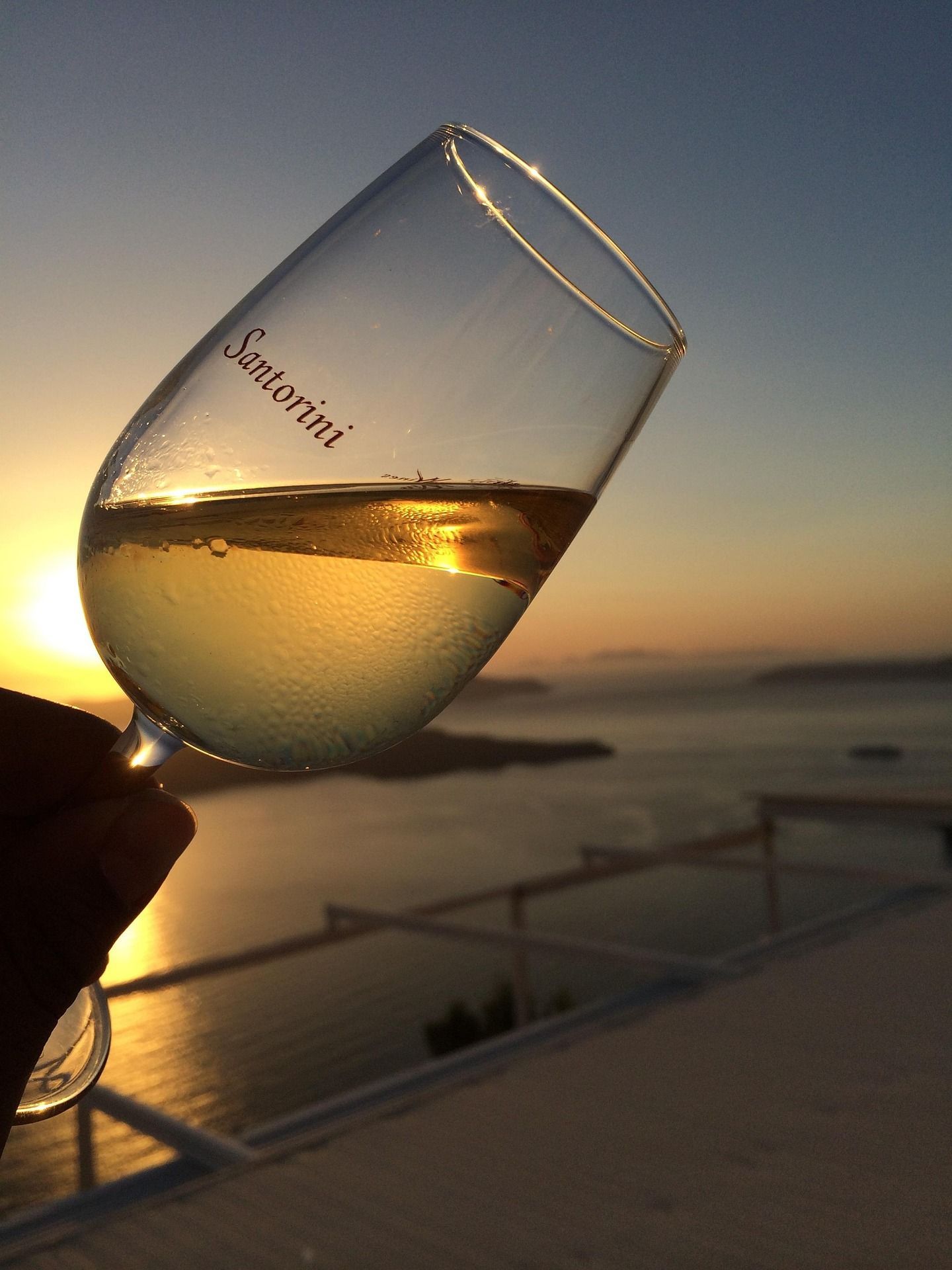 Hand holding a tilted wine glass at sunset overlooking the sea