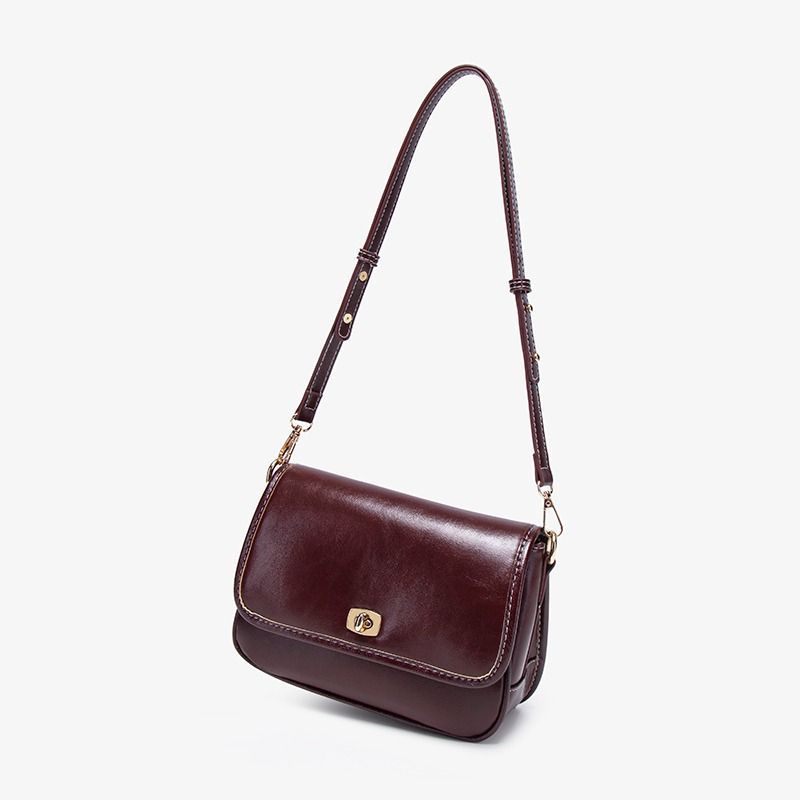 Bolso de hombro de piel marrón oscuro con correa larga, cierre dorado y costuras blancas.