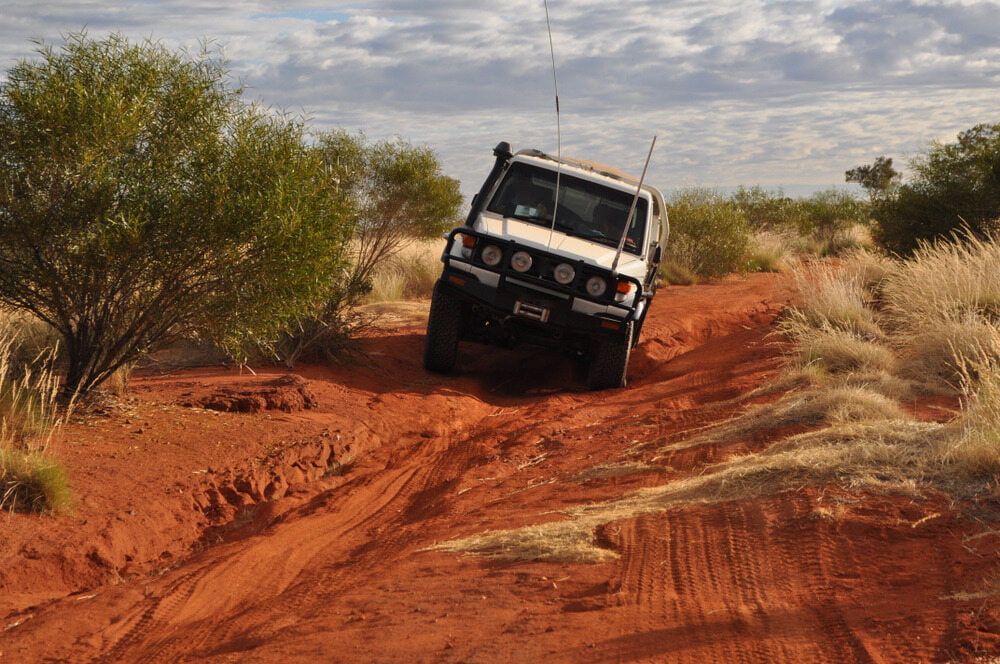 A White SUV Is Driving Down A Dirt Road In The Desert — Wilson's Towing In Roma, QLD