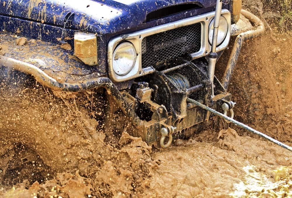 A Blue Jeep Is Stuck In The Mud With A Winch Attached To It — Wilson's Towing In Gatton, QLD