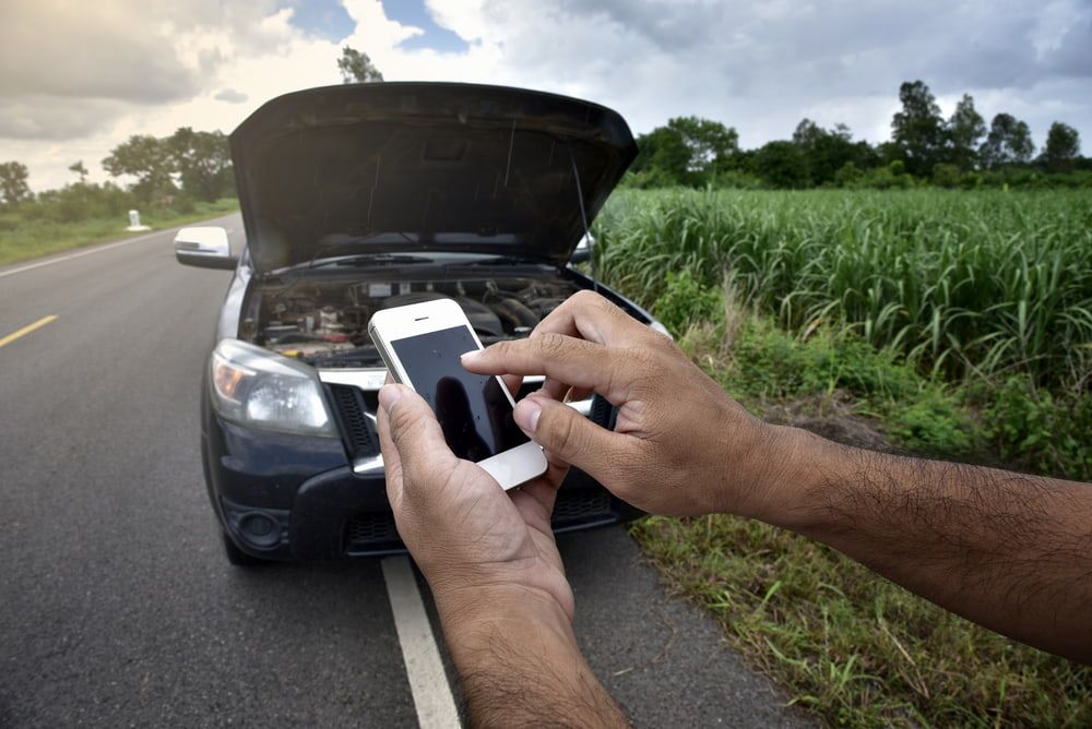 A Person Is Holding A Cell Phone In Front Of A Broken Down Car — Wilson's Towing In North Toowoomba, QLD