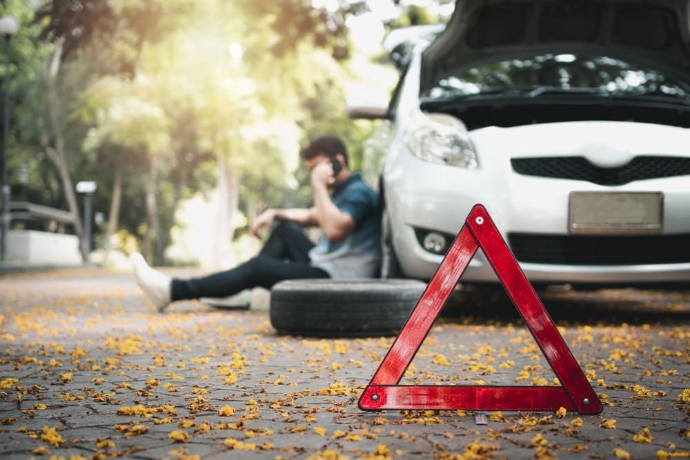 A Man Is Sitting On The Ground Next To A Broken Down Car — Wilson's Towing In Miles, QLD