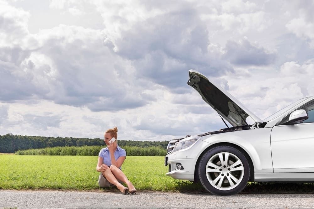 A Woman Is Sitting On The Side Of The Road Next To A Broken Down Car — Wilson's Towing In Goondiwindi, QLD