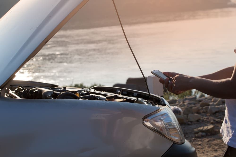 A Person Is Standing Next To A Broken Down Car With The Hood Open And Using A Cell Phone — Wilson's Towing In Roma, QLD