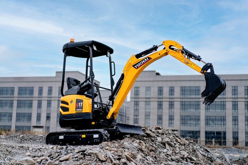 Yellow YUCHAI U17 excavator on a pile of rubble in front of a building.