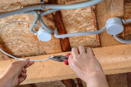 A person from Nick’s Electrical LLC is cutting a wire with a pair of pliers.