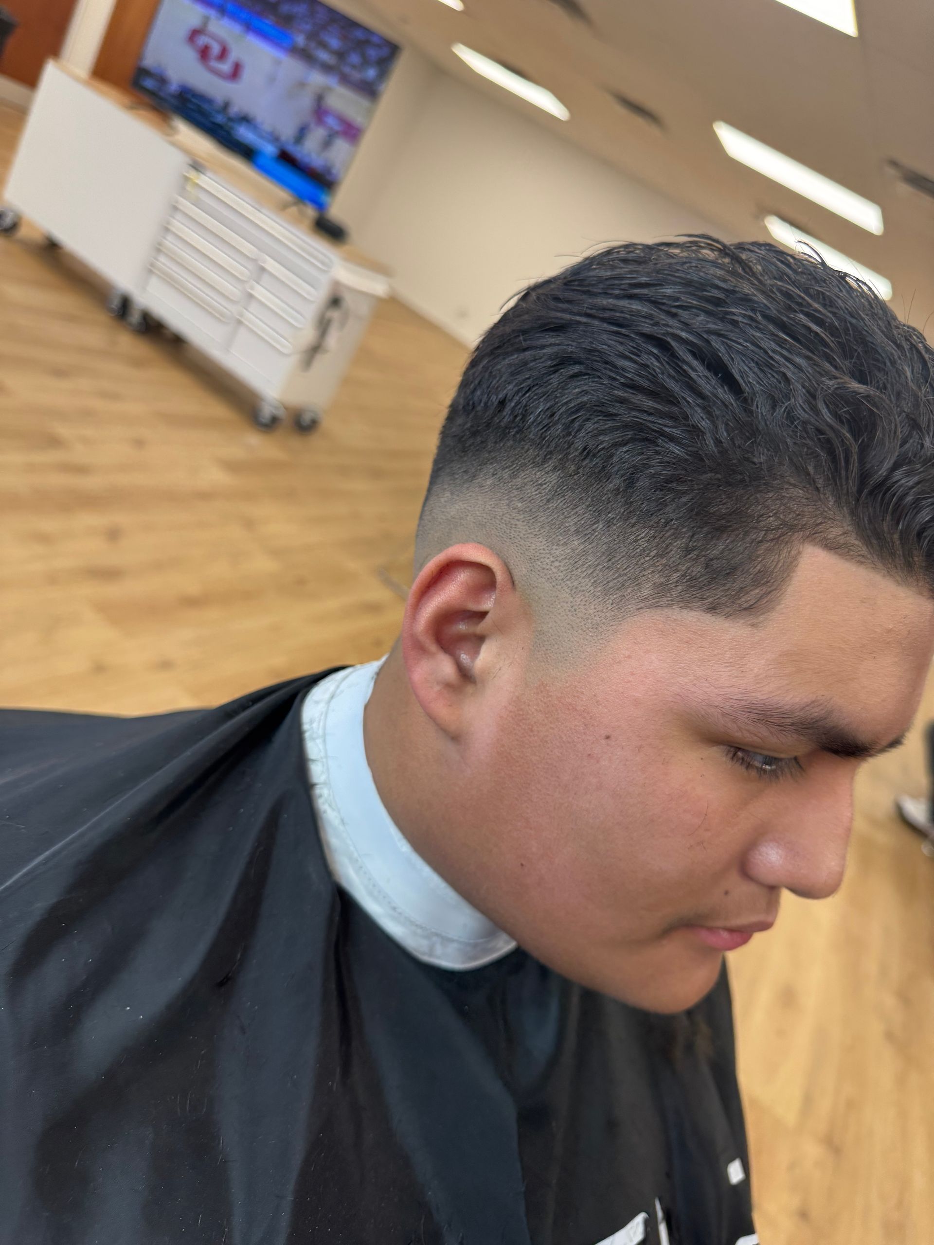 A close-up profile view of a person with a fresh, short fade haircut, shown inside a barbershop.
