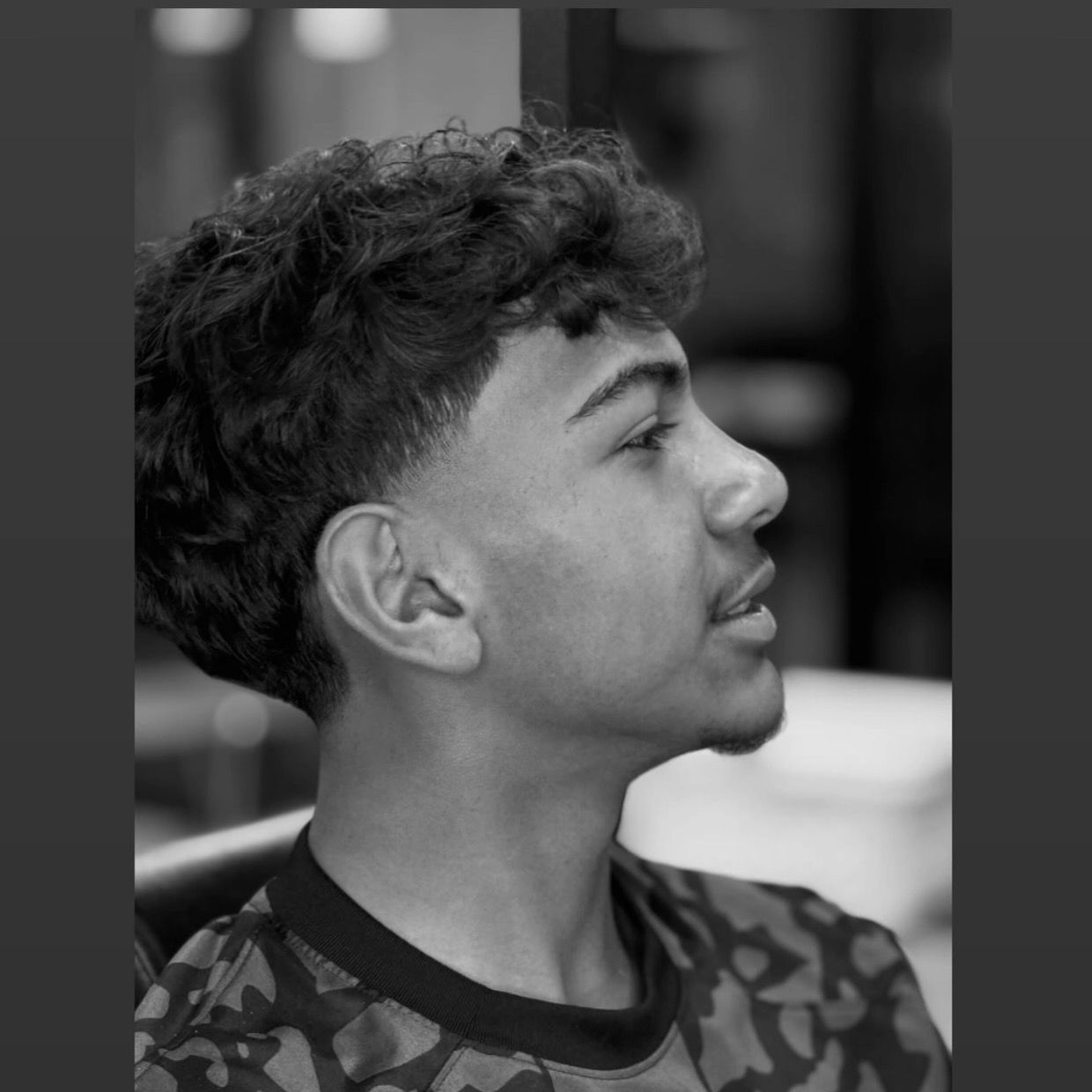 A profile view of a person with a curly top hairstyle and a skin fade, wearing a patterned shirt.