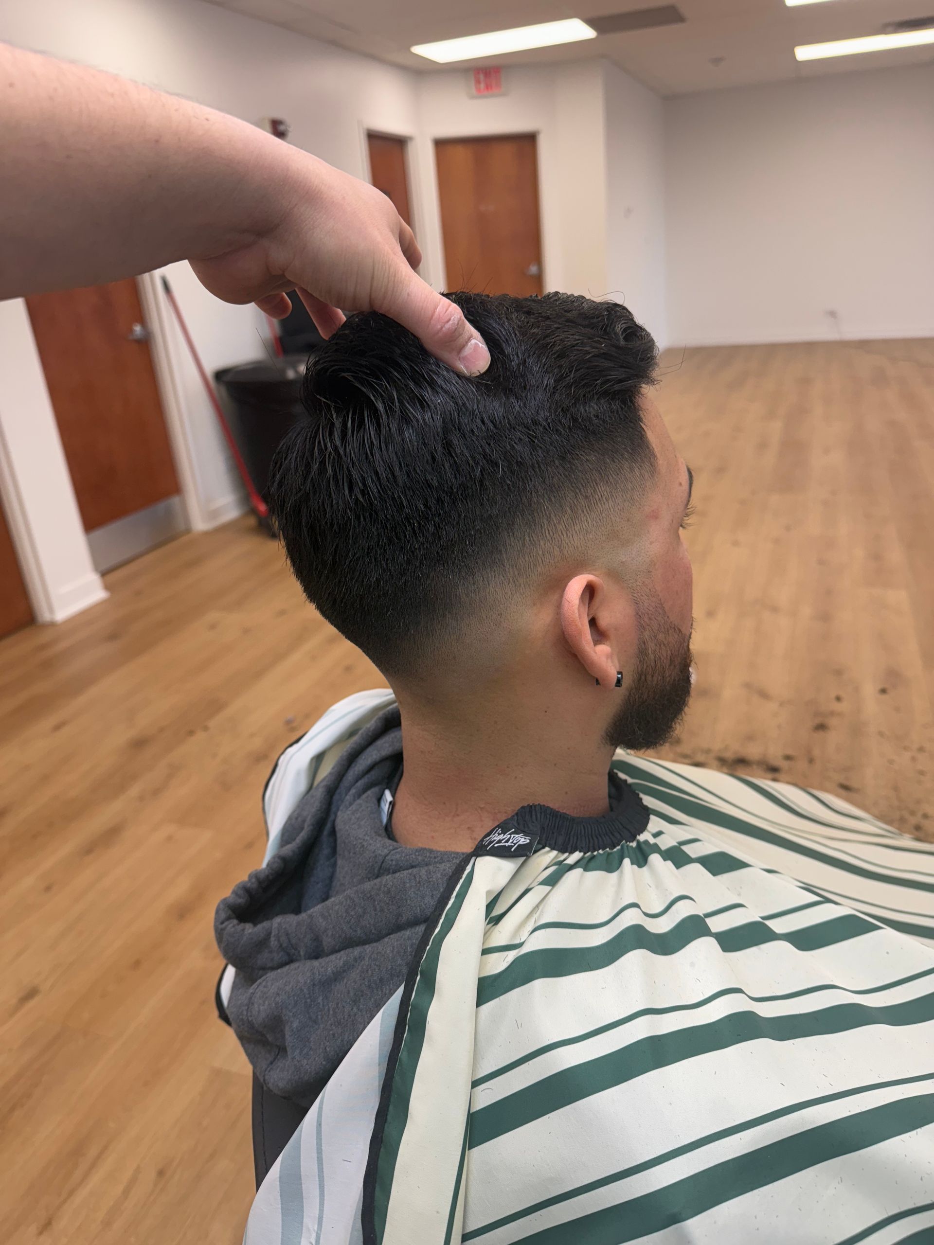 A person holding a client's hair to display a fresh skin fade haircut in a barbershop.