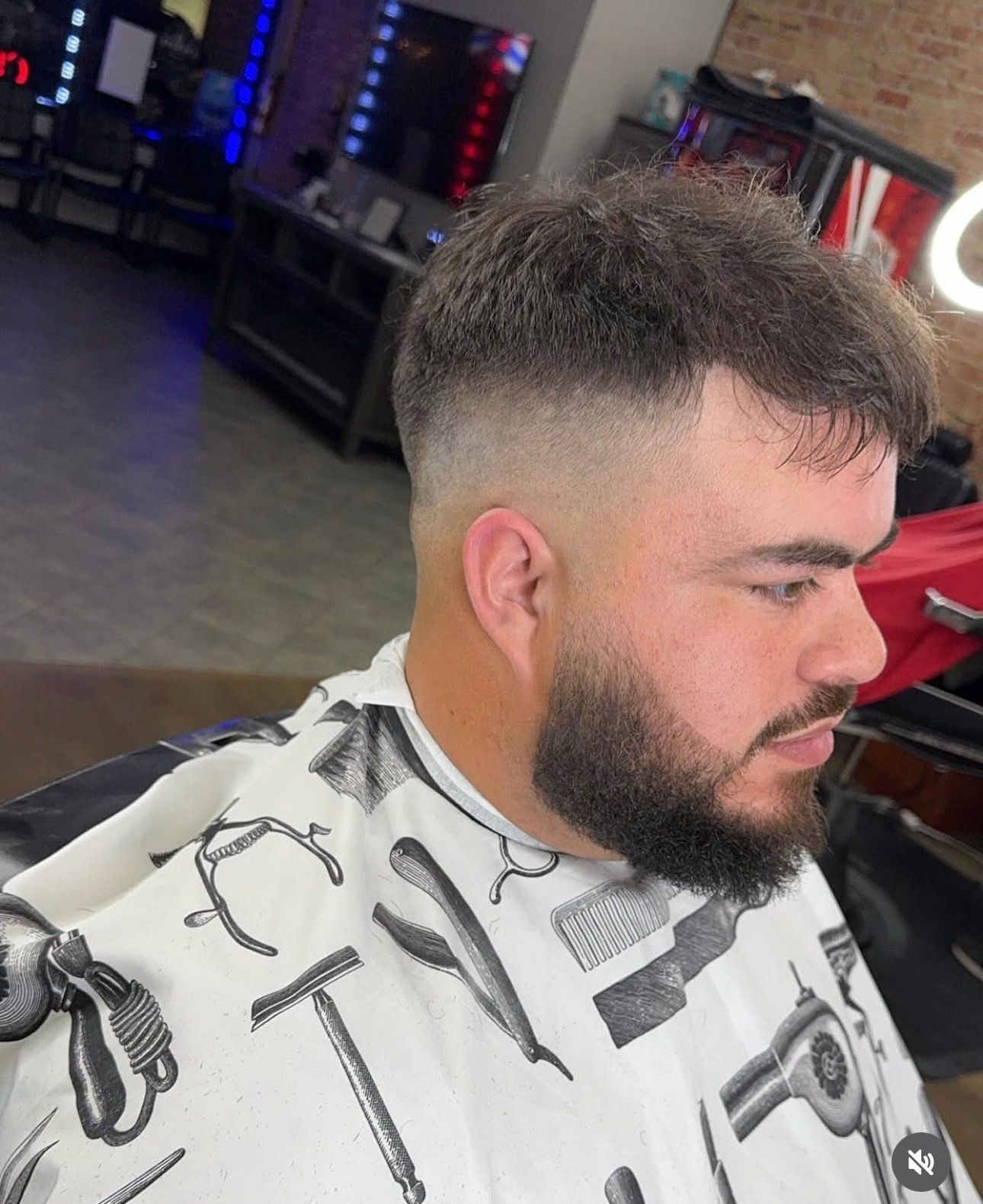 A person with a short, textured top haircut featuring a faded side, wearing a barber’s cape in a salon setting.