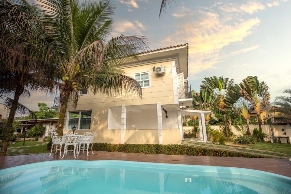 Uma casa grande com uma piscina na frente, cercada por palmeiras.