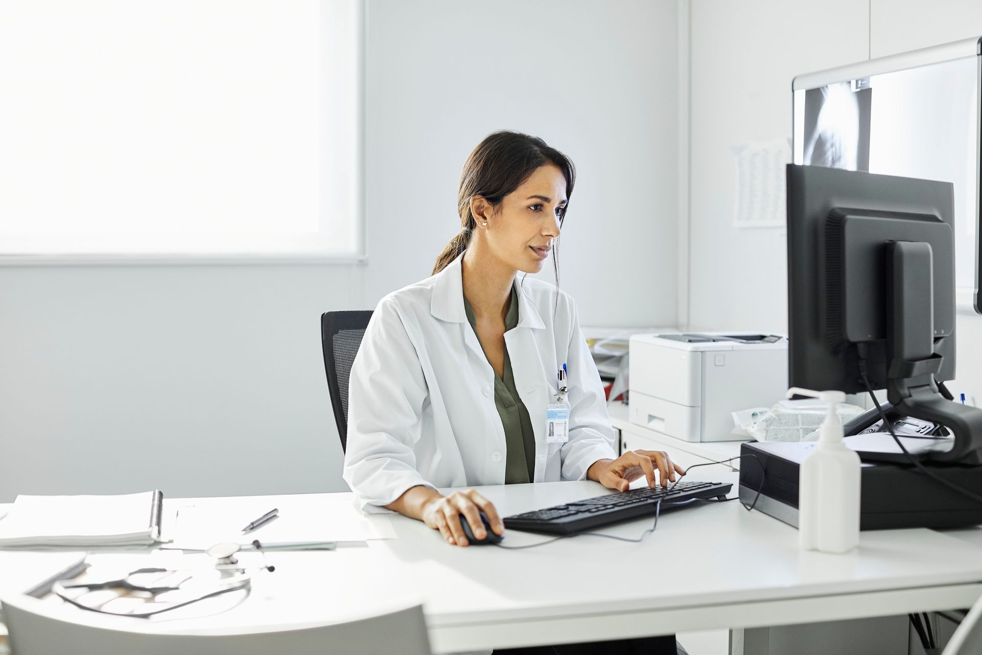 Doctor in a white coat working at a computer in a bright office. Doctor in a white coat working at a computer in a bright office.