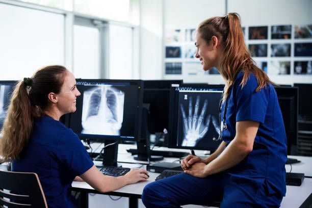 Two medical professionals in blue scrubs reviewing X-rays on computer monitors.
