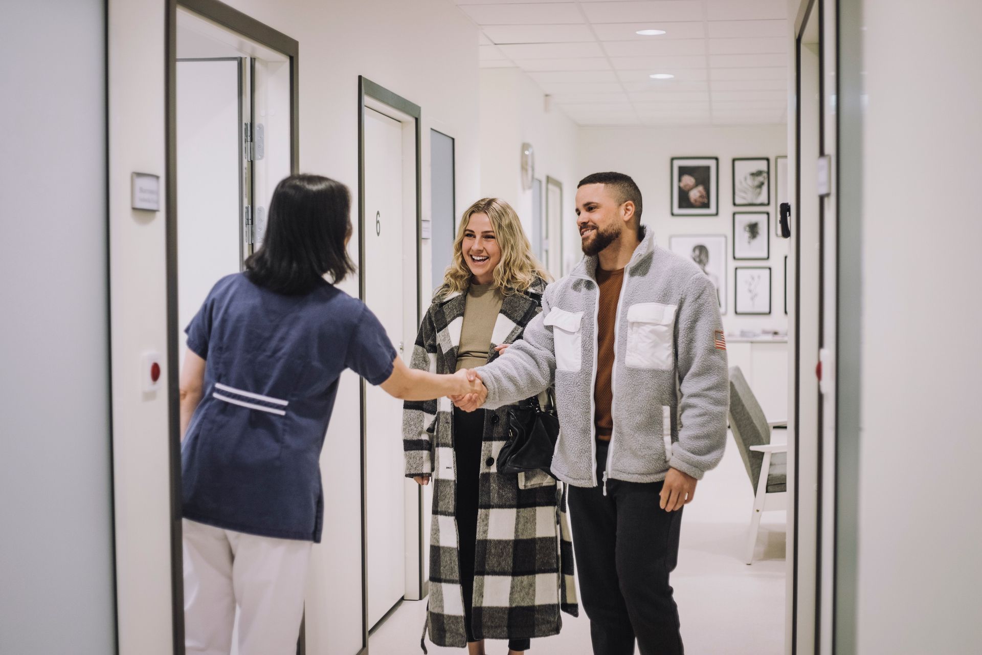A healthcare worker shakes hands with a couple in a clinic hallway.