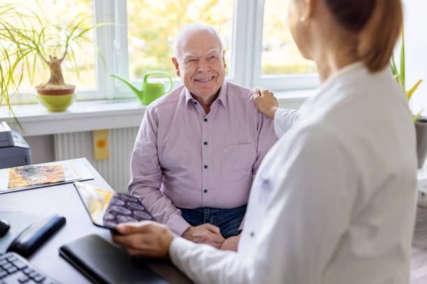 Doctor comforts patient in office, smiling. Hand on shoulder. Sunlight through window.
