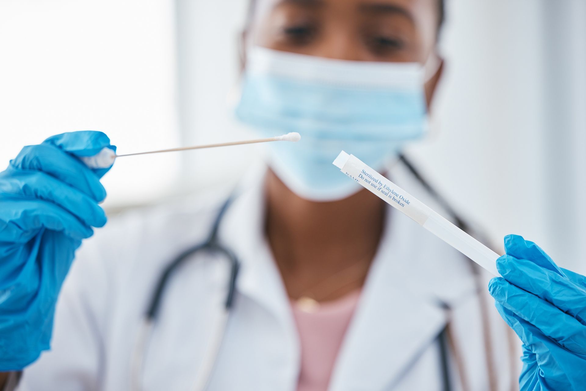 Medical professional wearing mask and gloves preparing a swab for a medical test.