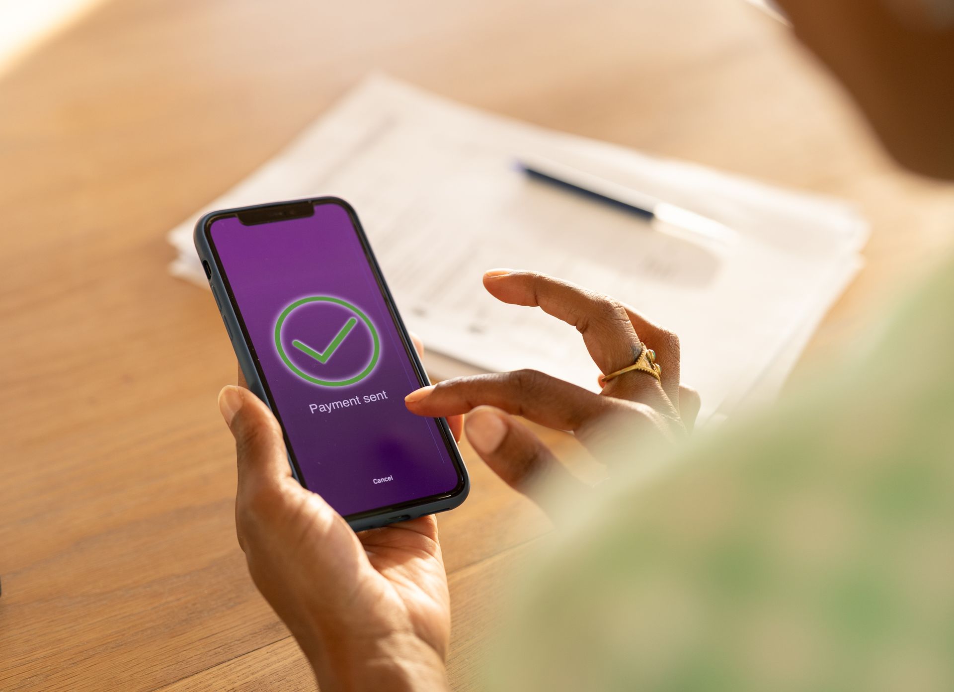 Person holding a smartphone displaying a checkmark on a purple screen, next to papers and a pen. Person holding a smartphone displaying a checkmark on a purple screen, next to papers and a pen.