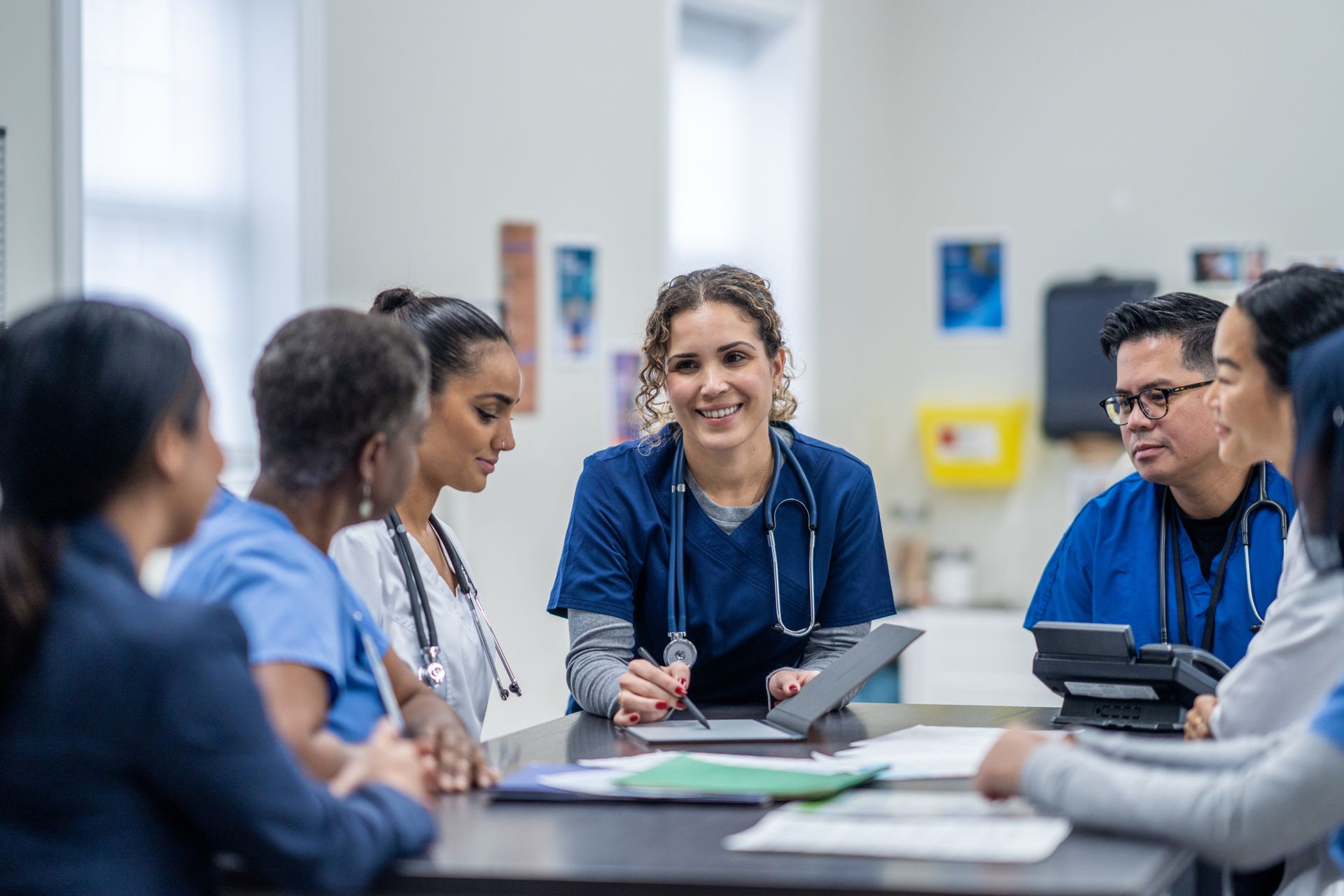 Medical team in blue scrubs at a table, smiling and looking at a tablet. Medical team in blue scrubs at a table, smiling and looking at a tablet.