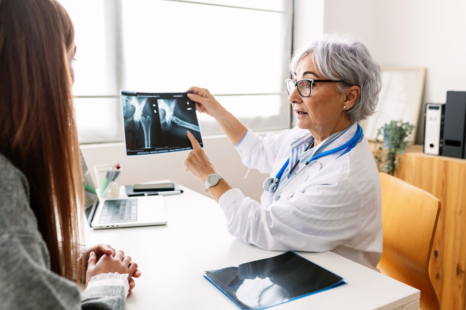 Doctor points to X-ray, explaining to patient at a desk in a medical office.