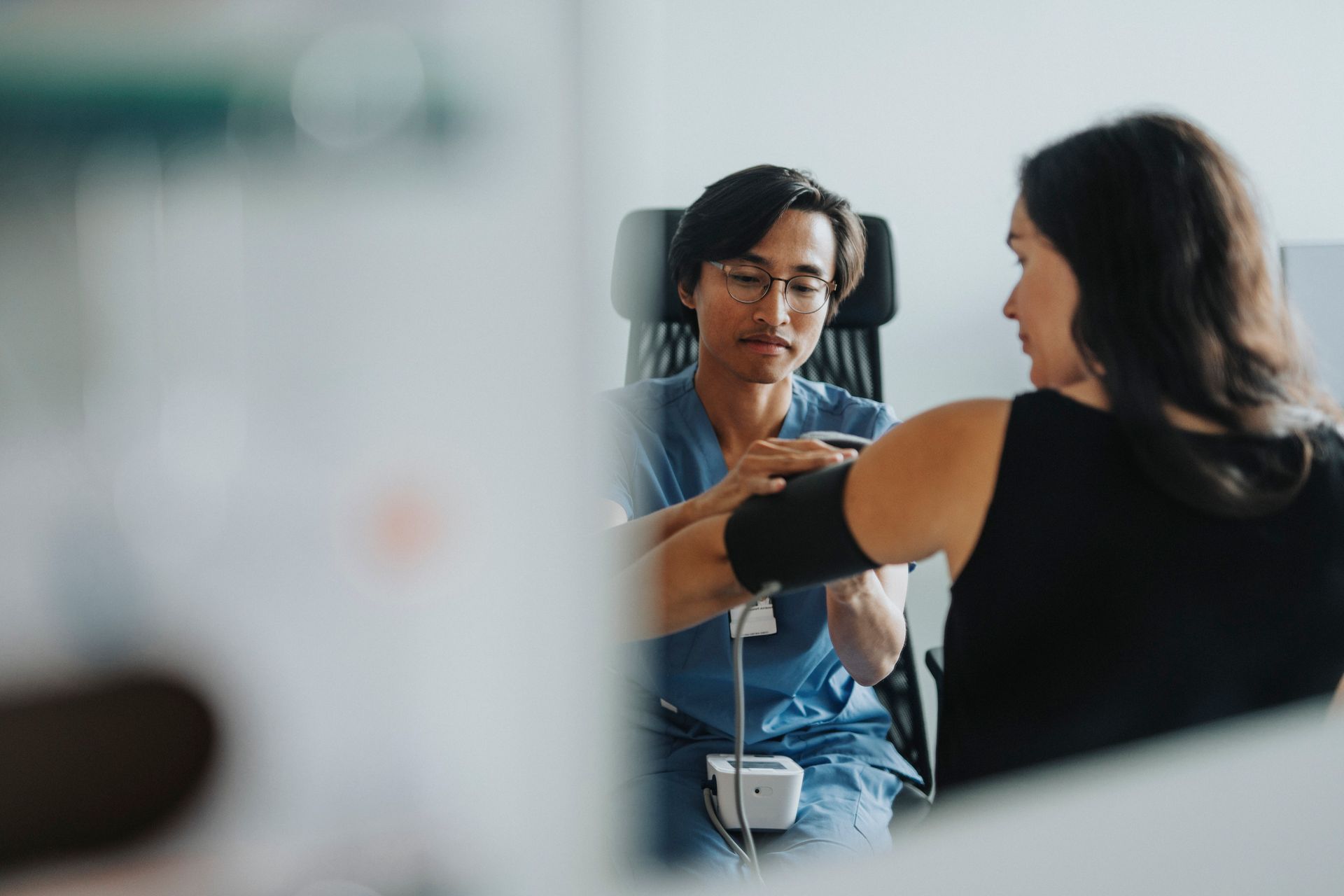Doctor taking patient's blood pressure in an office. Doctor is wearing glasses and a blue uniform.