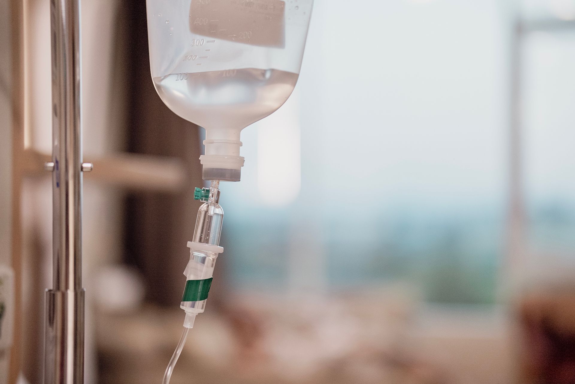 IV drip bag with clear liquid hanging in a hospital room. IV drip bag with clear liquid hanging in a hospital room.
