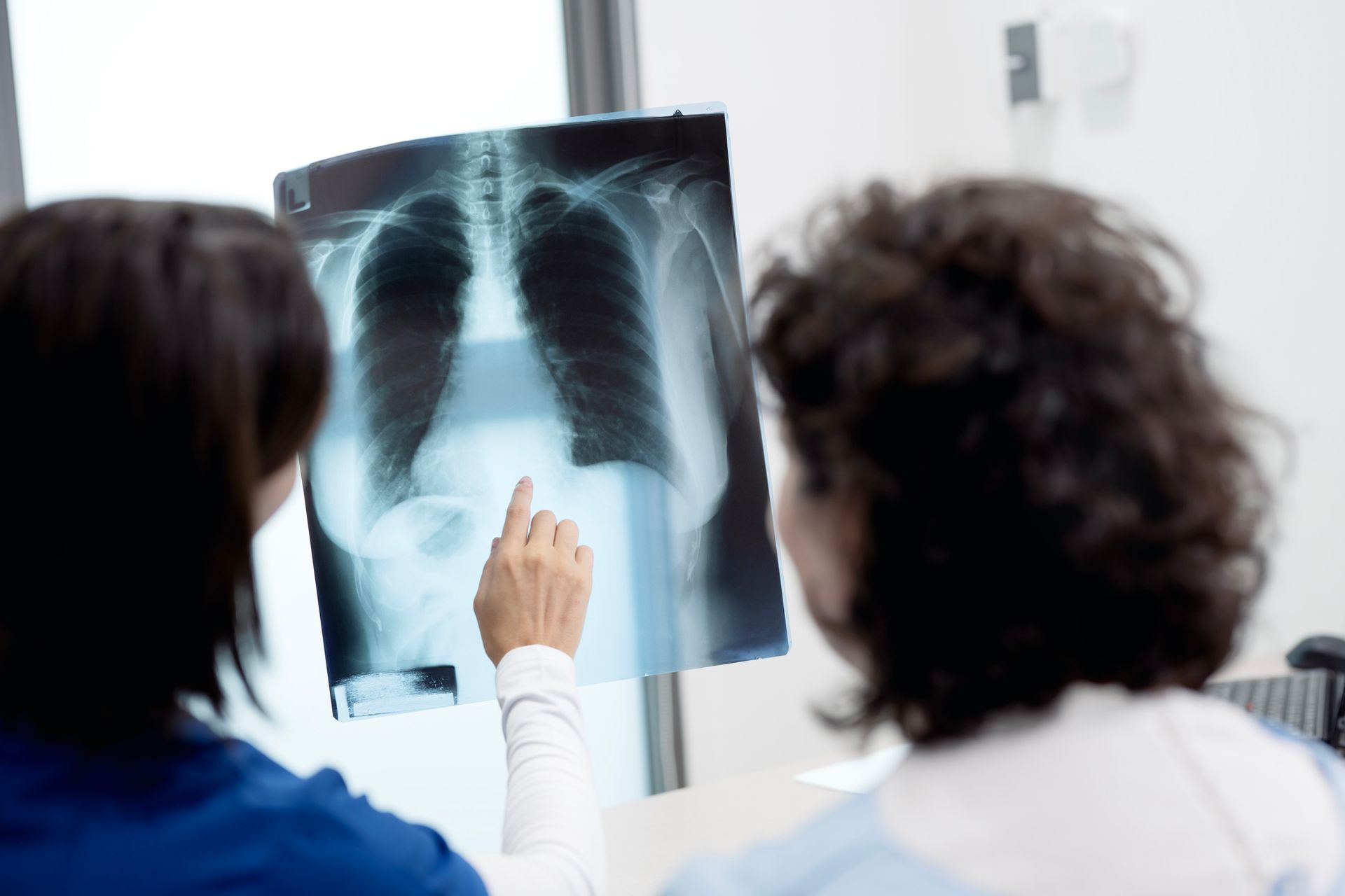 Two medical professionals examining a chest X-ray in a clinical setting. Two medical professionals examining a chest X-ray in a clinical setting.