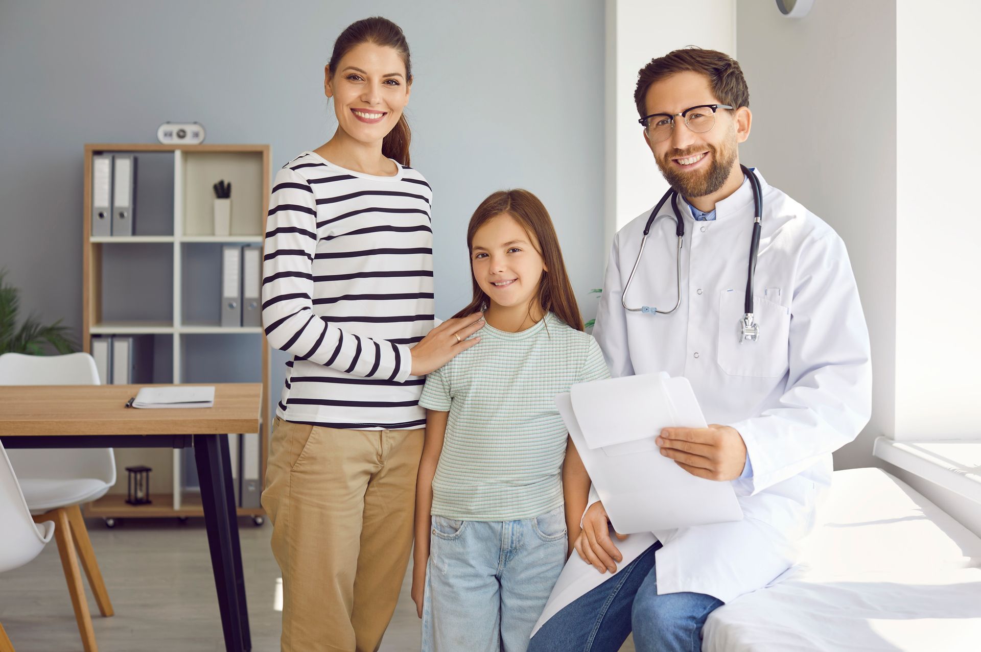 A mother, daughter, and doctor smiling at the camera in a doctor's office.