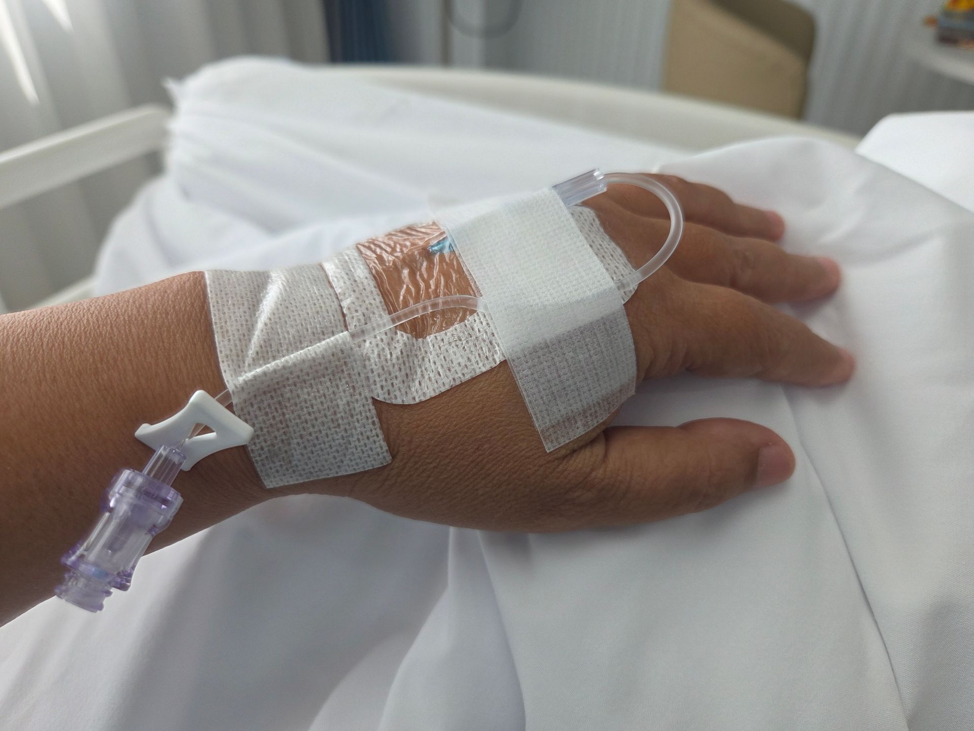 Hand with IV in hospital bed, taped to the wrist. Hand with IV in hospital bed, taped to the wrist.