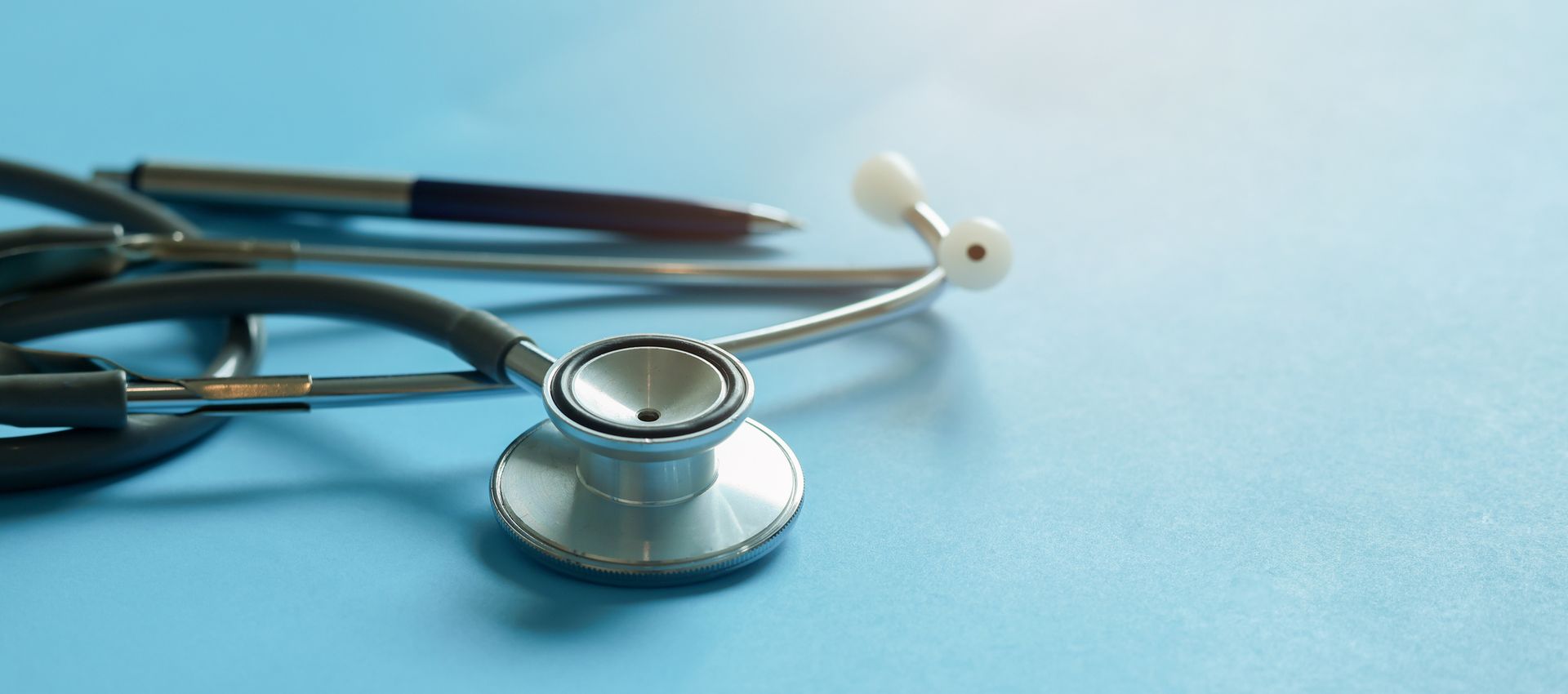 A stethoscope and pen on a light blue surface.