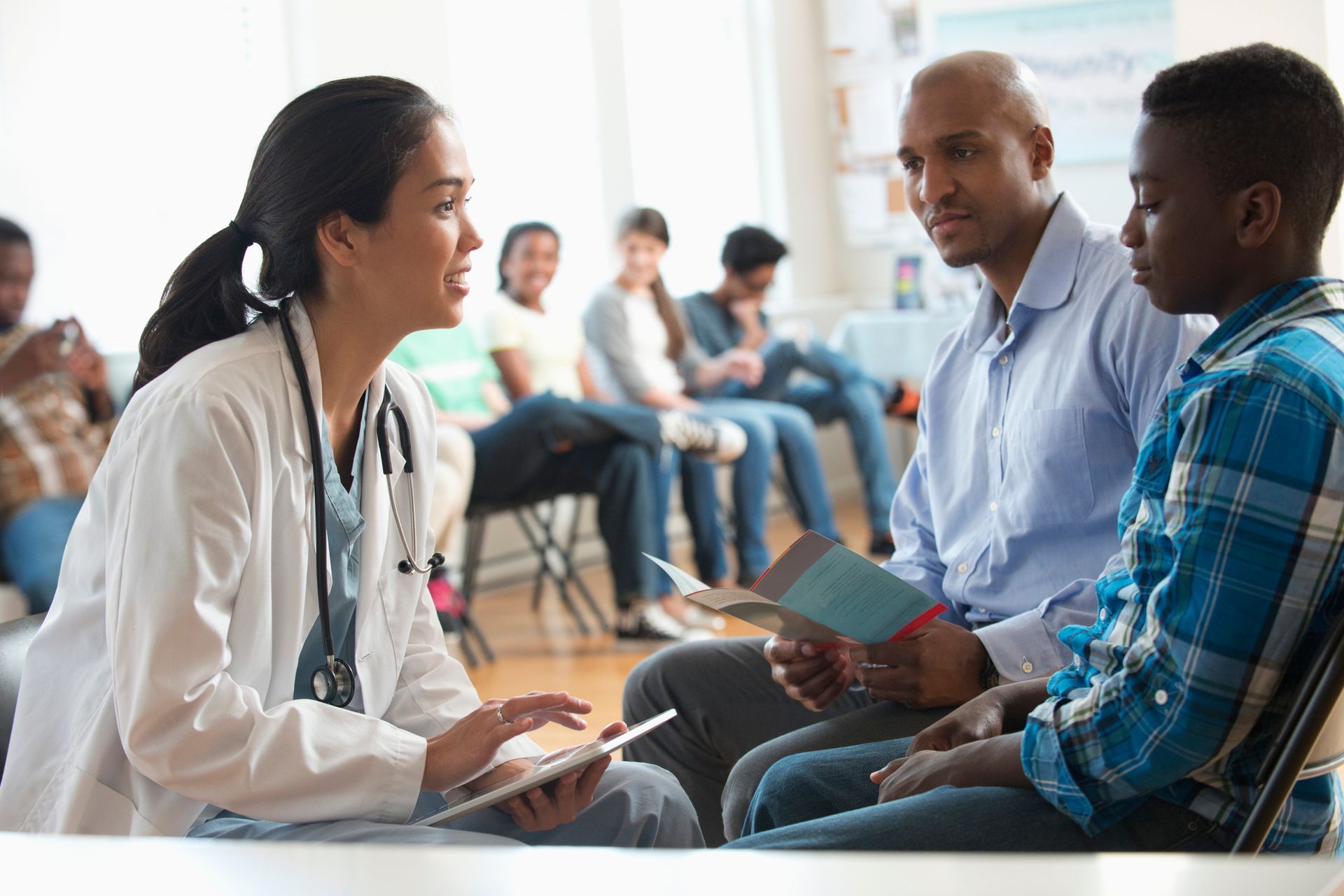 Doctor consults with a patient and parent in a waiting room. Doctor consults with a patient and parent in a waiting room.