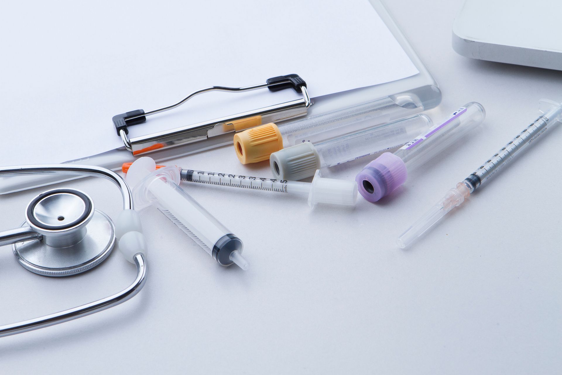 Medical equipment: stethoscope, clipboard, syringes, and vials on a white surface.