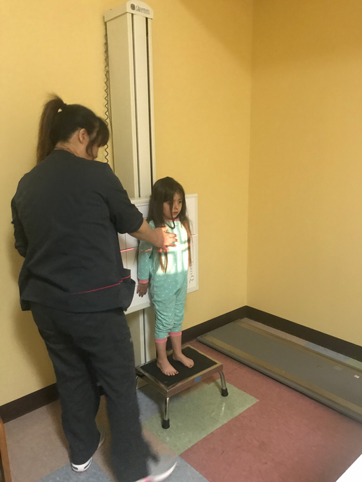 A child standing in front of a medical imaging machine, being assisted by a person in scrubs.