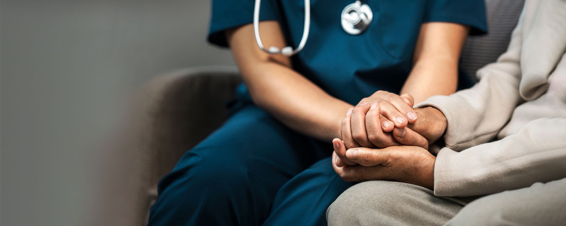 Nurse in blue scrubs holds the hands of an elderly person, showing comfort and support.